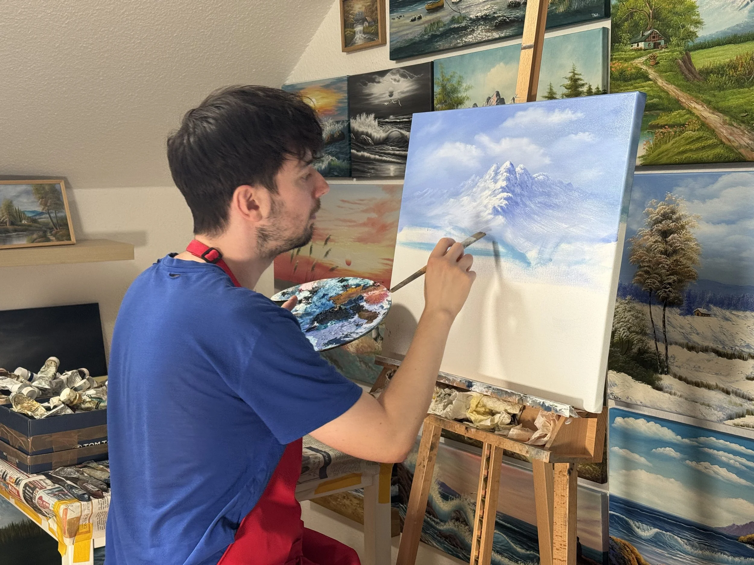 Tobias Nolte malt eine Berglandschaft auf Leinwand mit Öl mit einem Pinsel in der Hand.