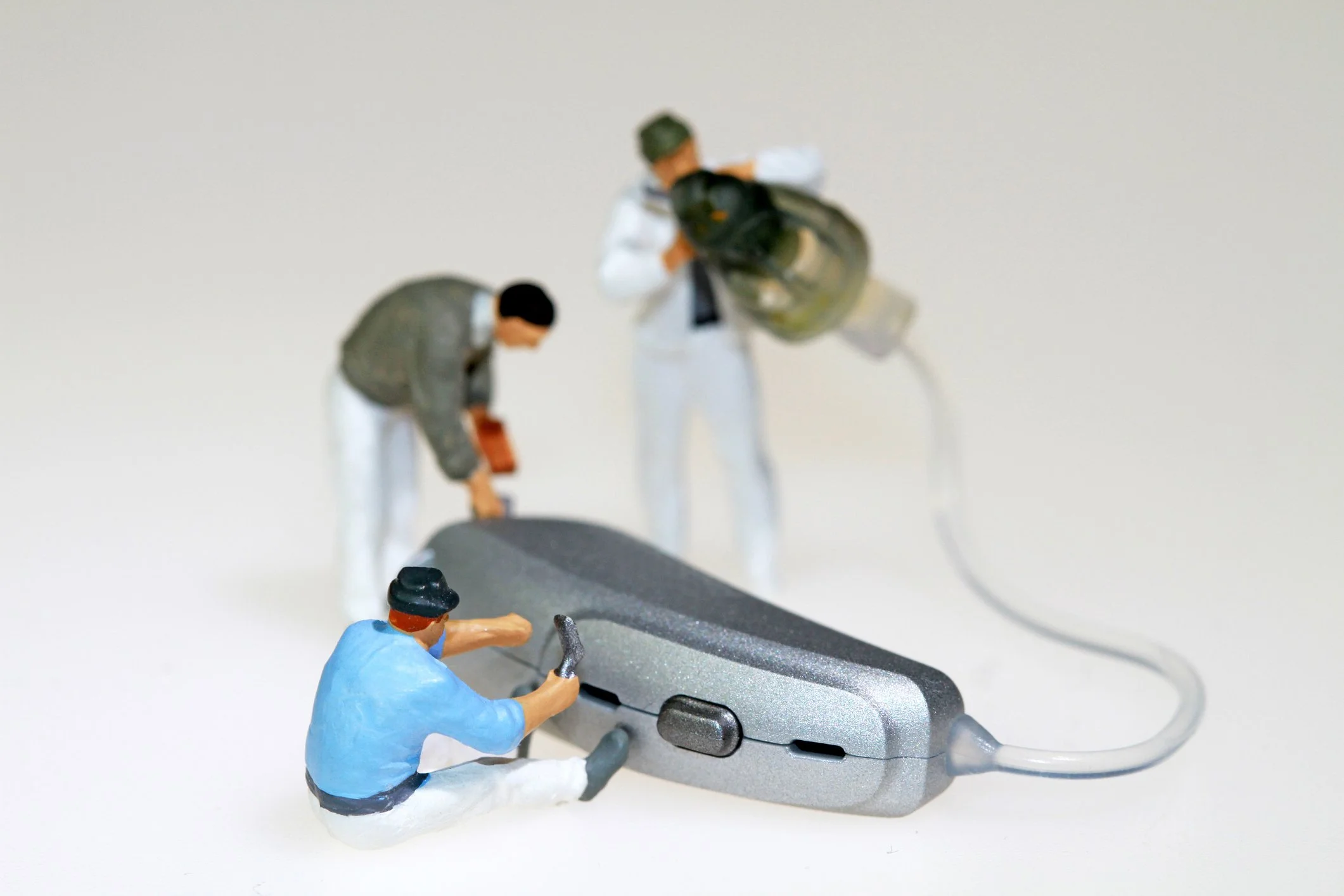 Miniature figurines of three workers repairing an electronic device, with a plain background.