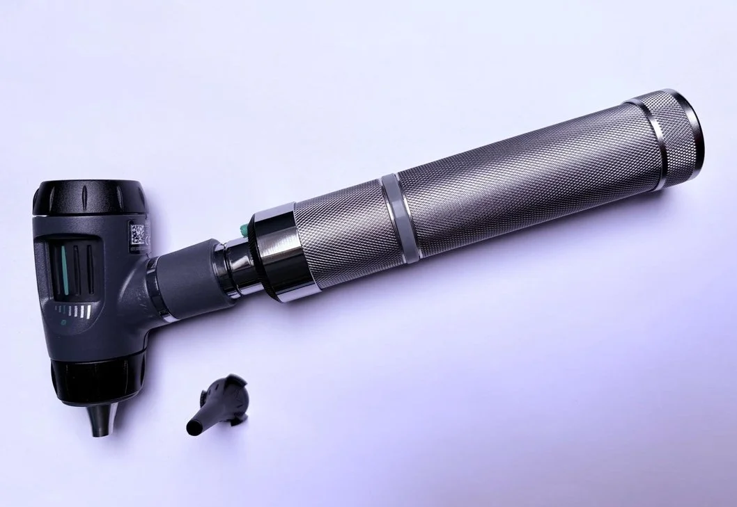 A gray and metallic tattoo removal laser device with a long, cylindrical, textured handpiece and a smaller, detachable tip, lying on a white surface.