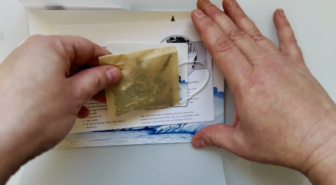 hands showing a tea bag and sticker being included with the package