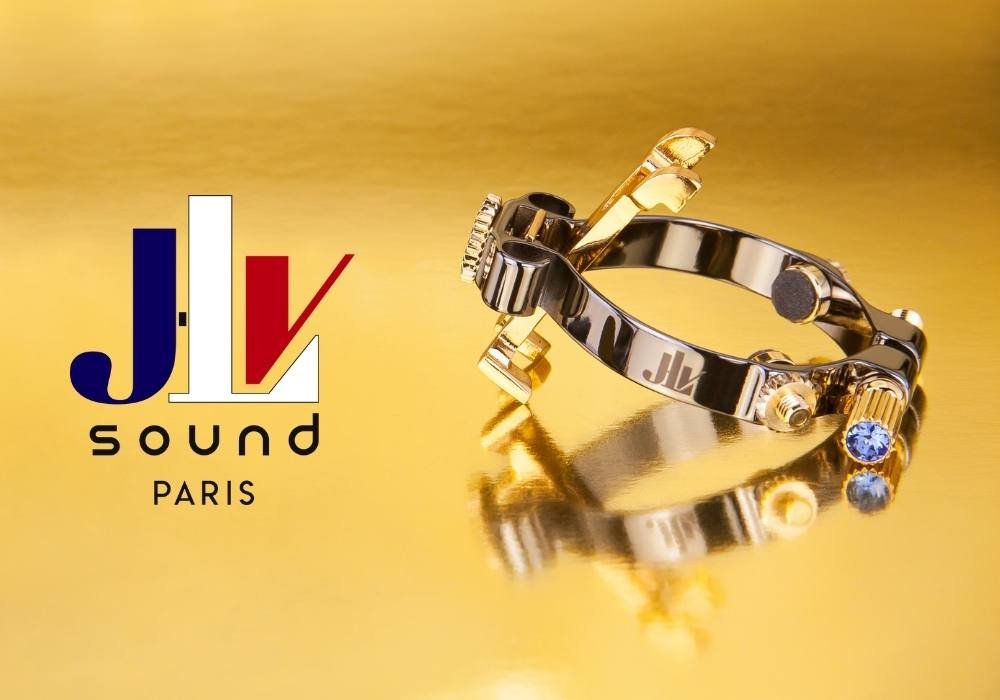 A gold and black ring with a blue gemstone placed on a reflective gold surface, with a Paris-based JLV Sound logo on the left.