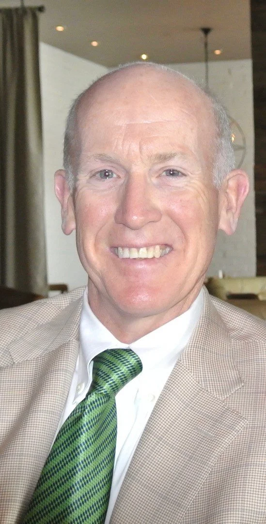 Brian smiling at the camera wearing a light suit with a green tie and white shirt.