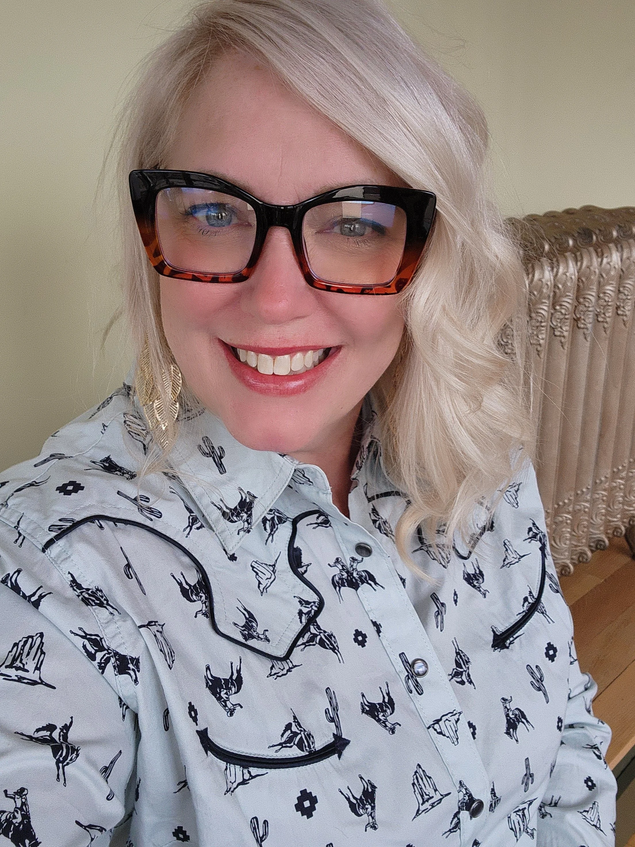 Katie smiling at the camera wearing a white patterned blouse with large ombre-shaded frames.
