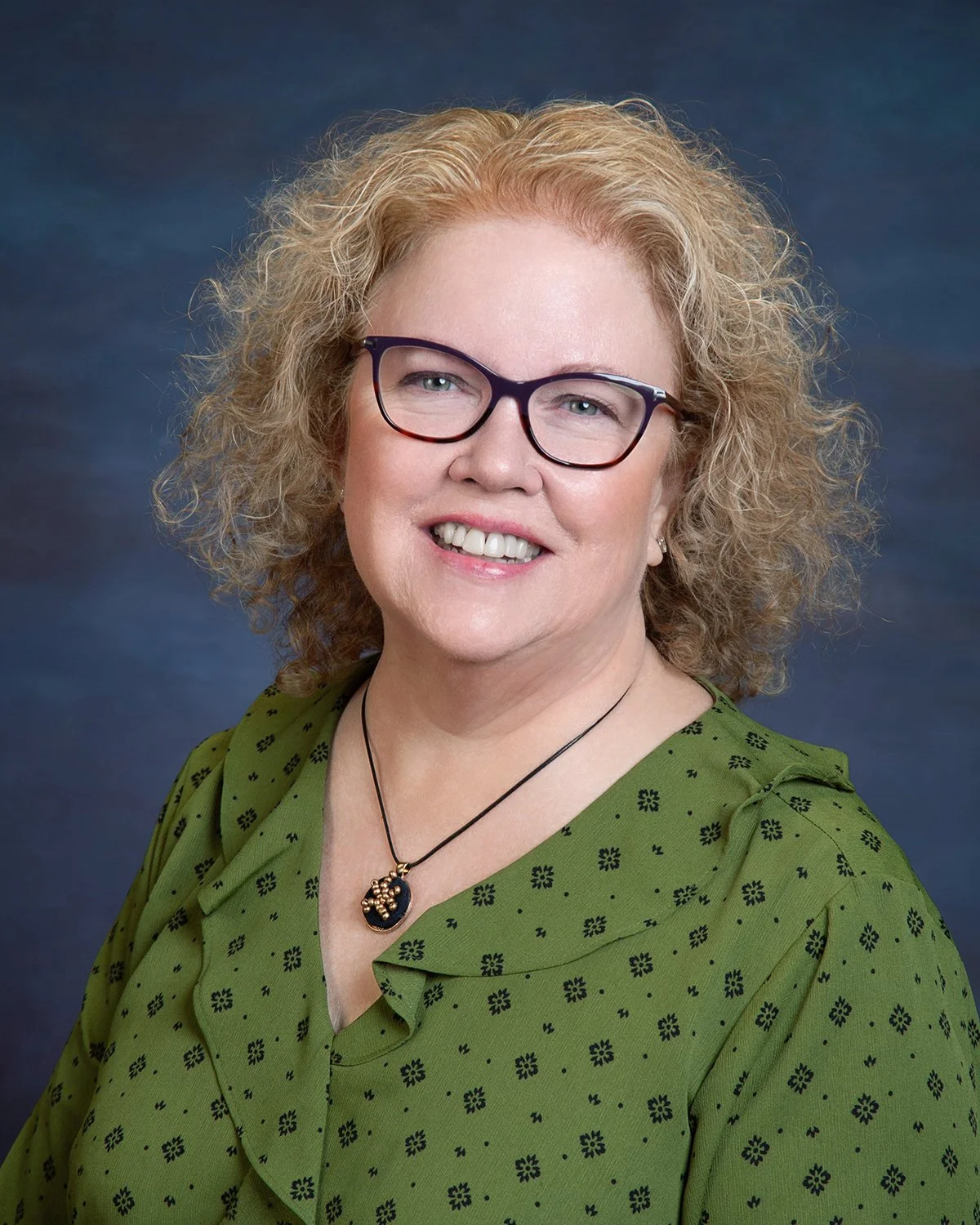 Kristi smiling at the camera wearing dark glasses and a green blouse.