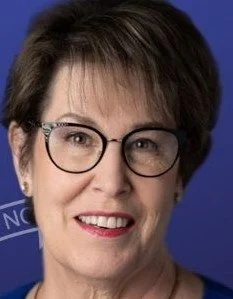 Teresa smiling at the camera wearing black, round framed glasses.