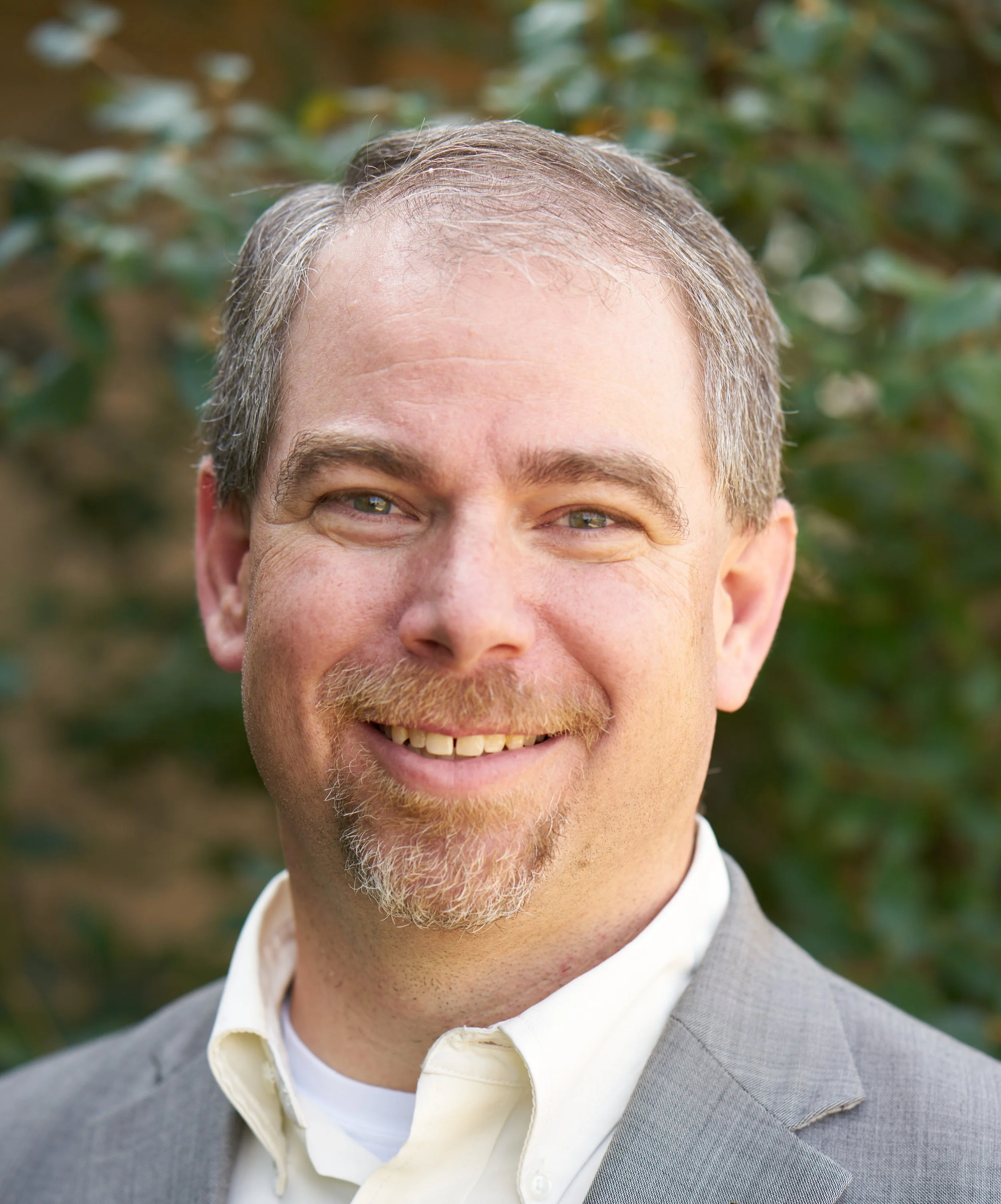 David smiling at the camera wearing a light grey suit with a cream dress shirt.