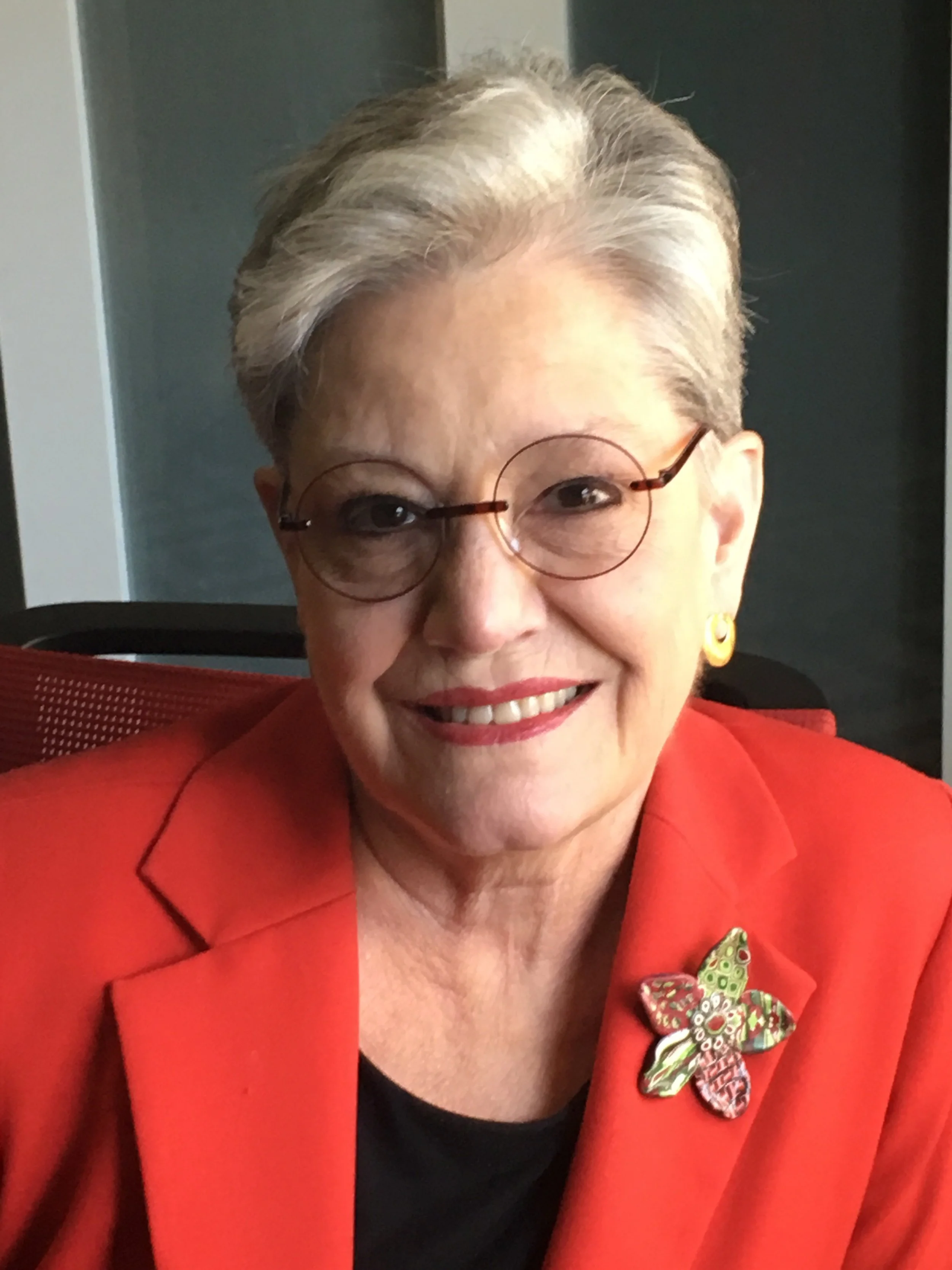 Terry smiling at the camera wearing round glasses an d a red blazer.