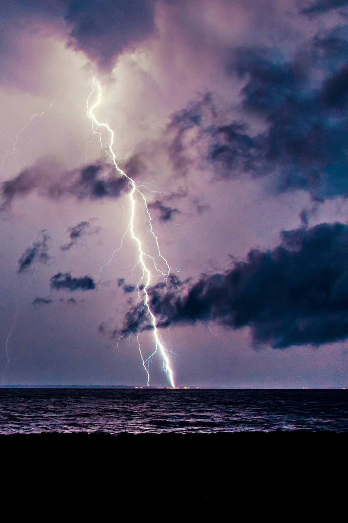 Lightning strikes over a stormy sky above the ocean.