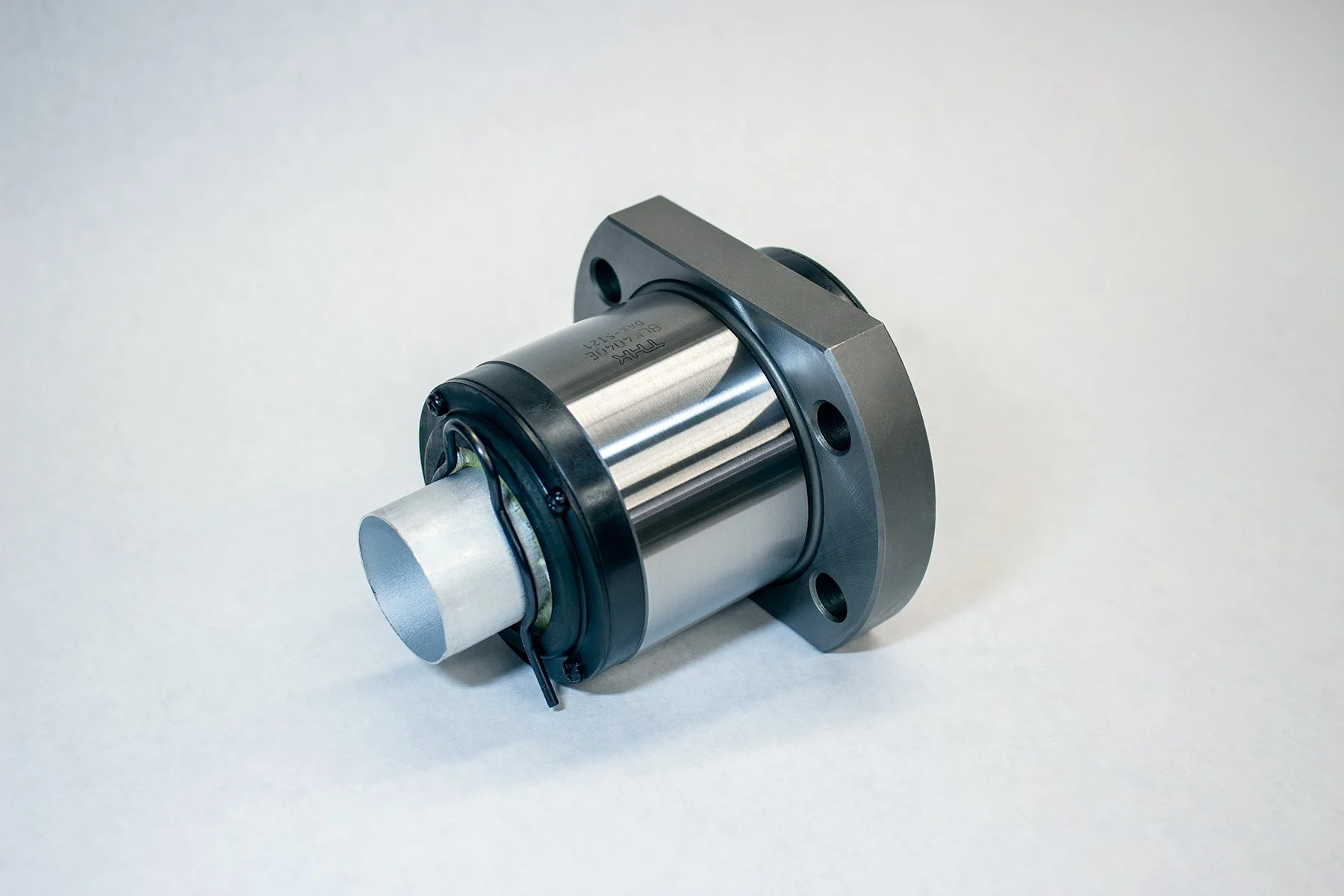 A metallic industrial component with a cylindrical shape and mounting flange, featuring visible screws and a black cable attached.