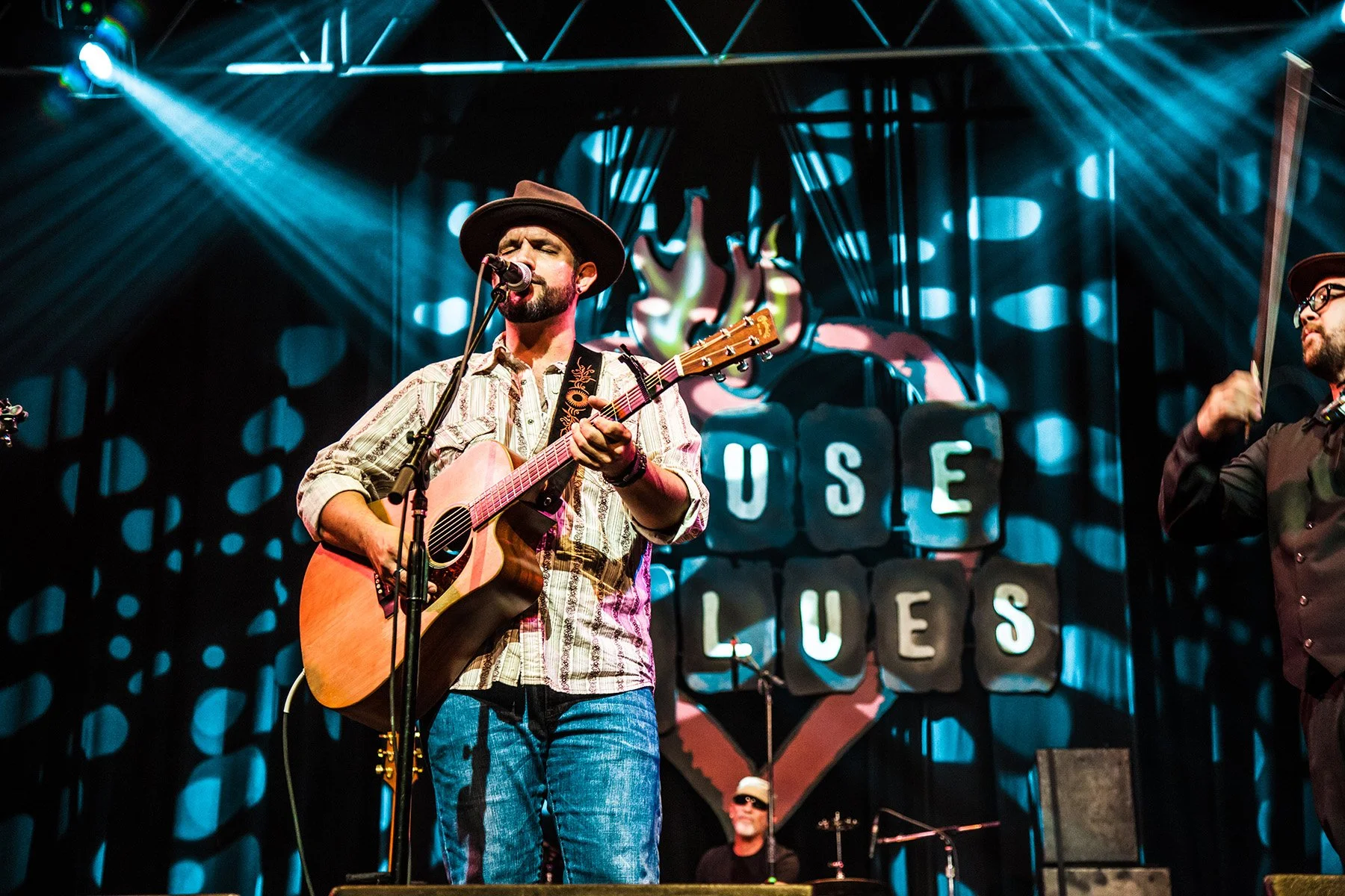 Musician singing and playing guitar on a stage with colorful lighting at the House of Blues.