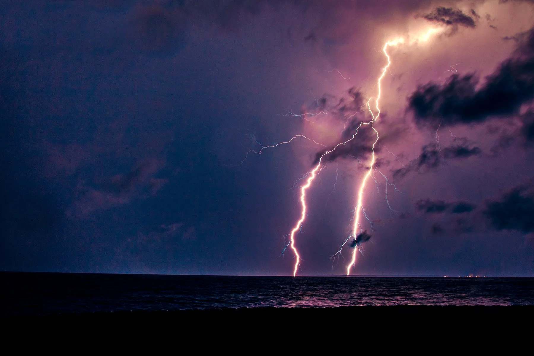 Lightning strikes over the ocean at night, illuminating the dark sky with bright flashes of electricity.