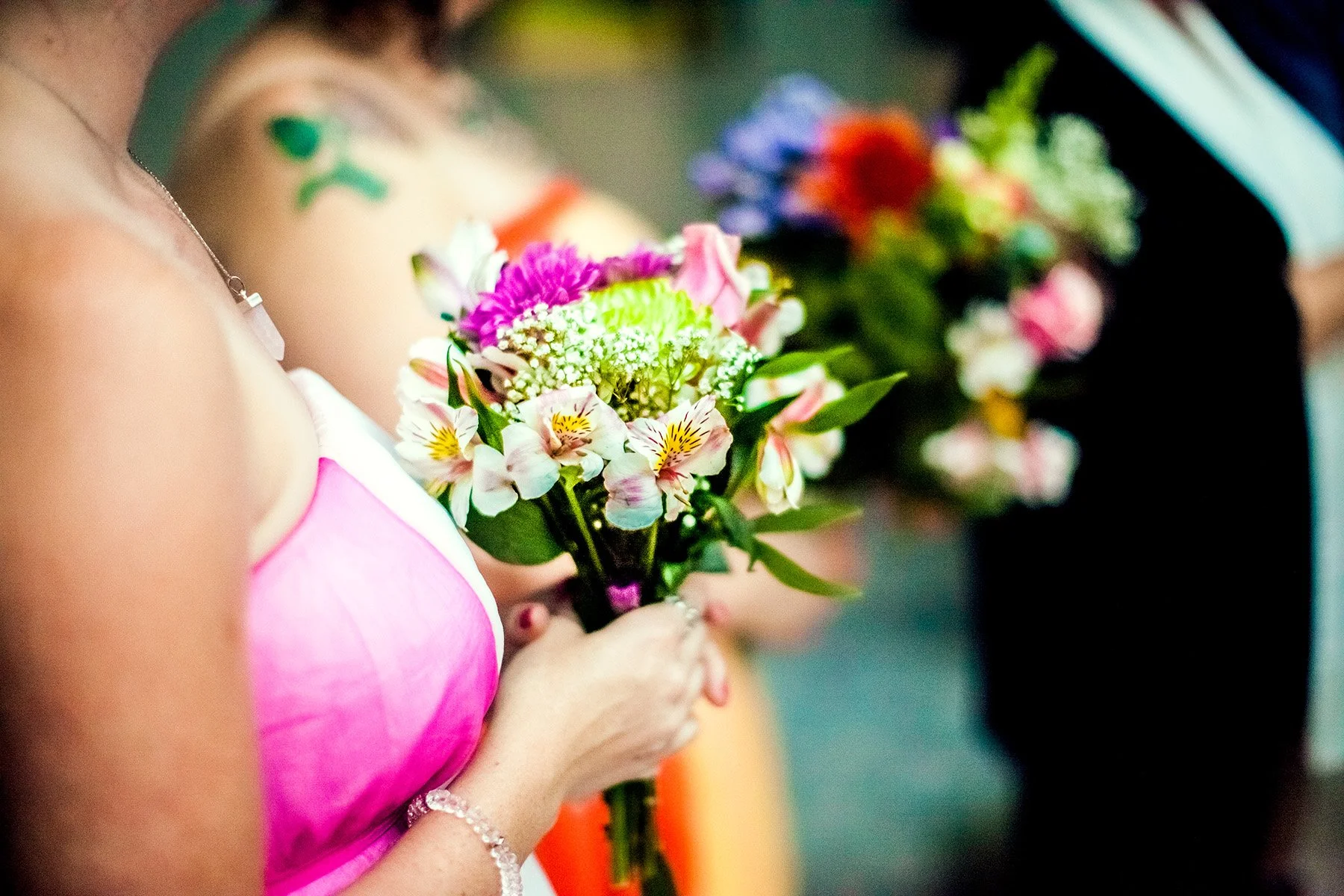 Close-up of women holding bouquets of colorful flowers during a celebration, with focus on the floral arrangements and festive attire.