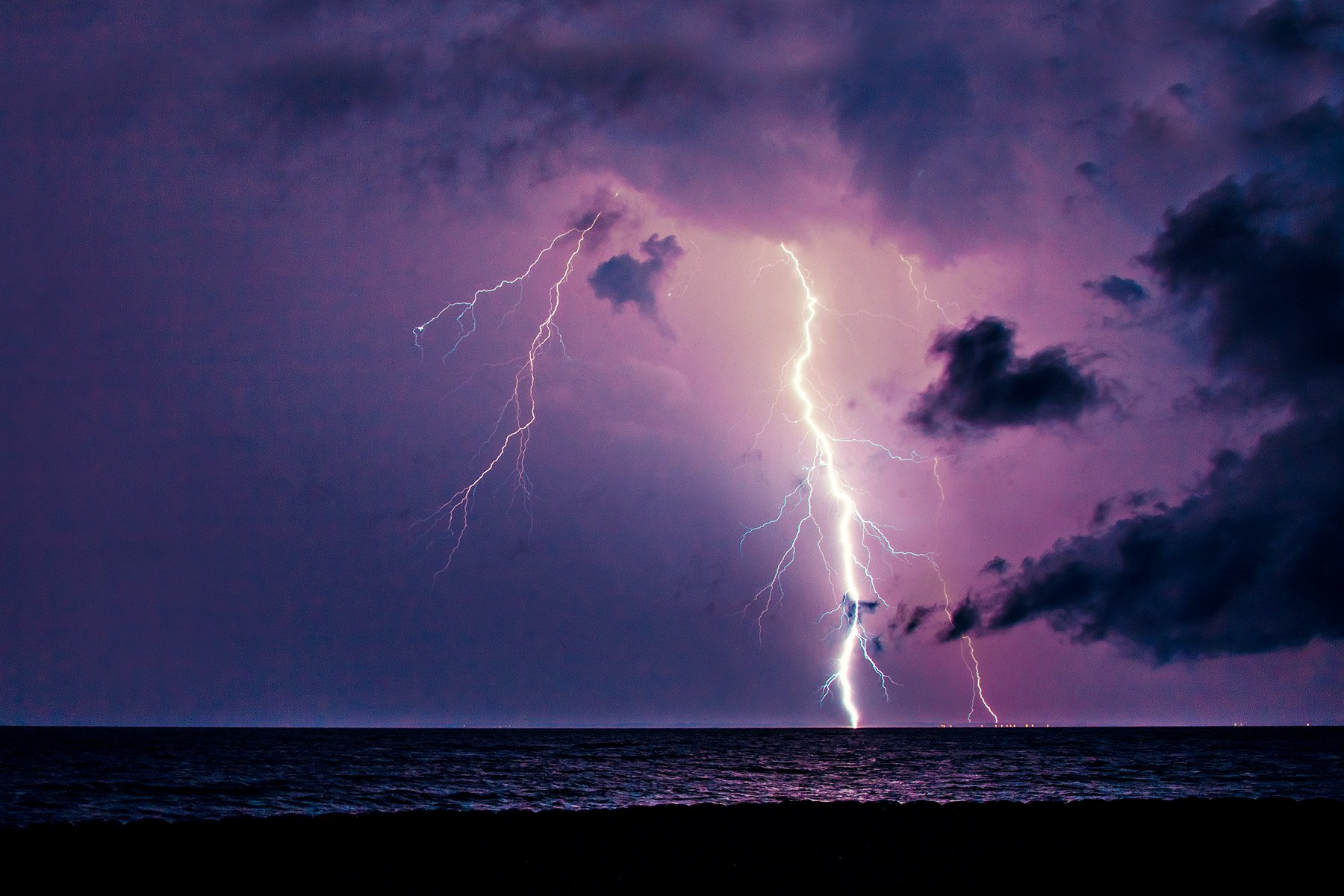 Lightning strikes over a dark ocean under a purple stormy sky.