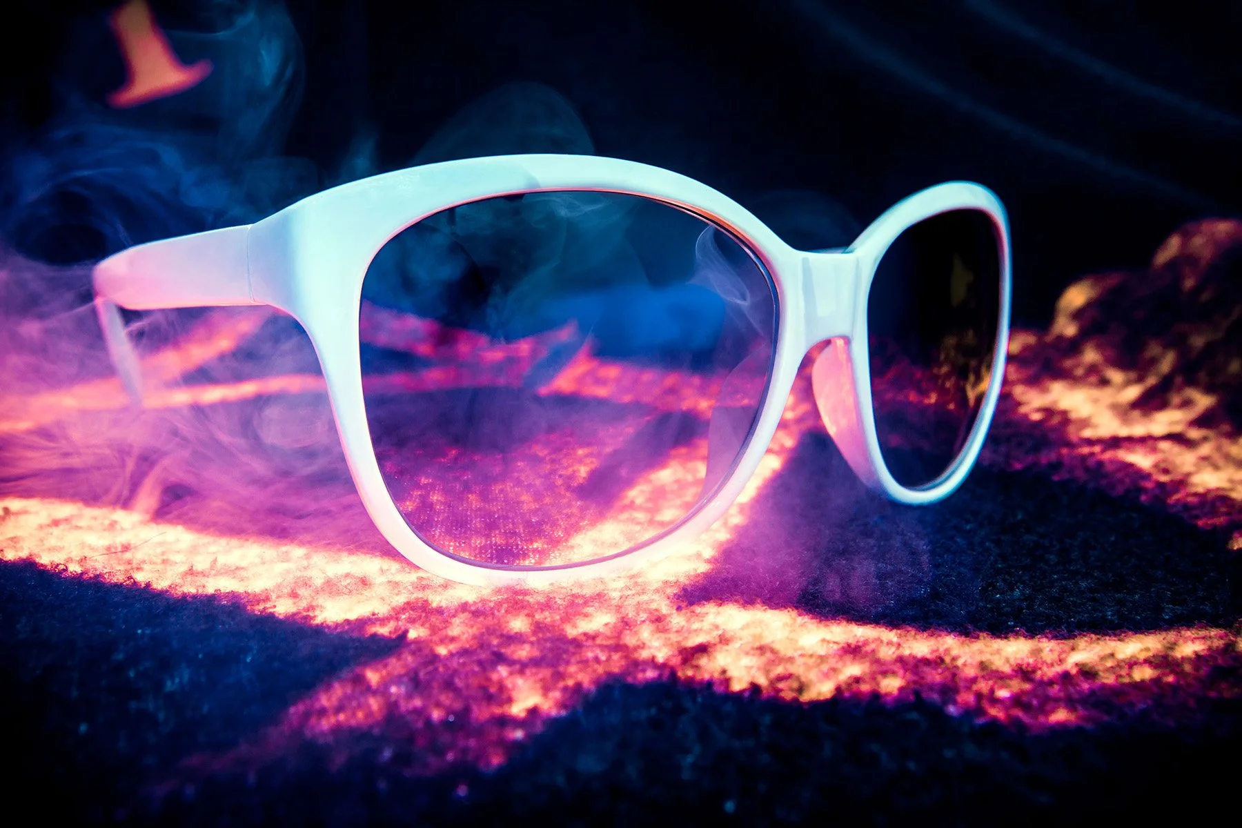 White sunglasses with reflective pink and purple lenses, placed on a surface with vibrant pink, purple, and blue lighting, and surrounded by smoke.