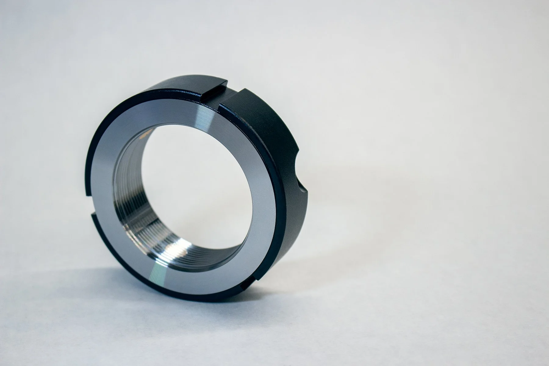 Close-up of a black and metallic circular mechanical component with inner threading, placed on a plain white background.