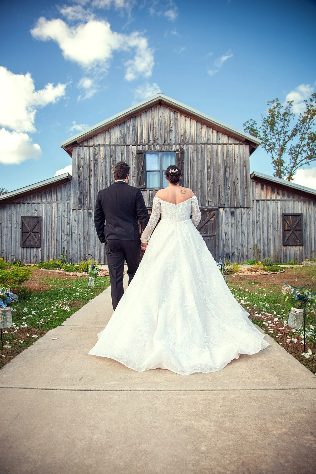 Bride and groom holding hands walking towards a wooden barn on a wedding day outside