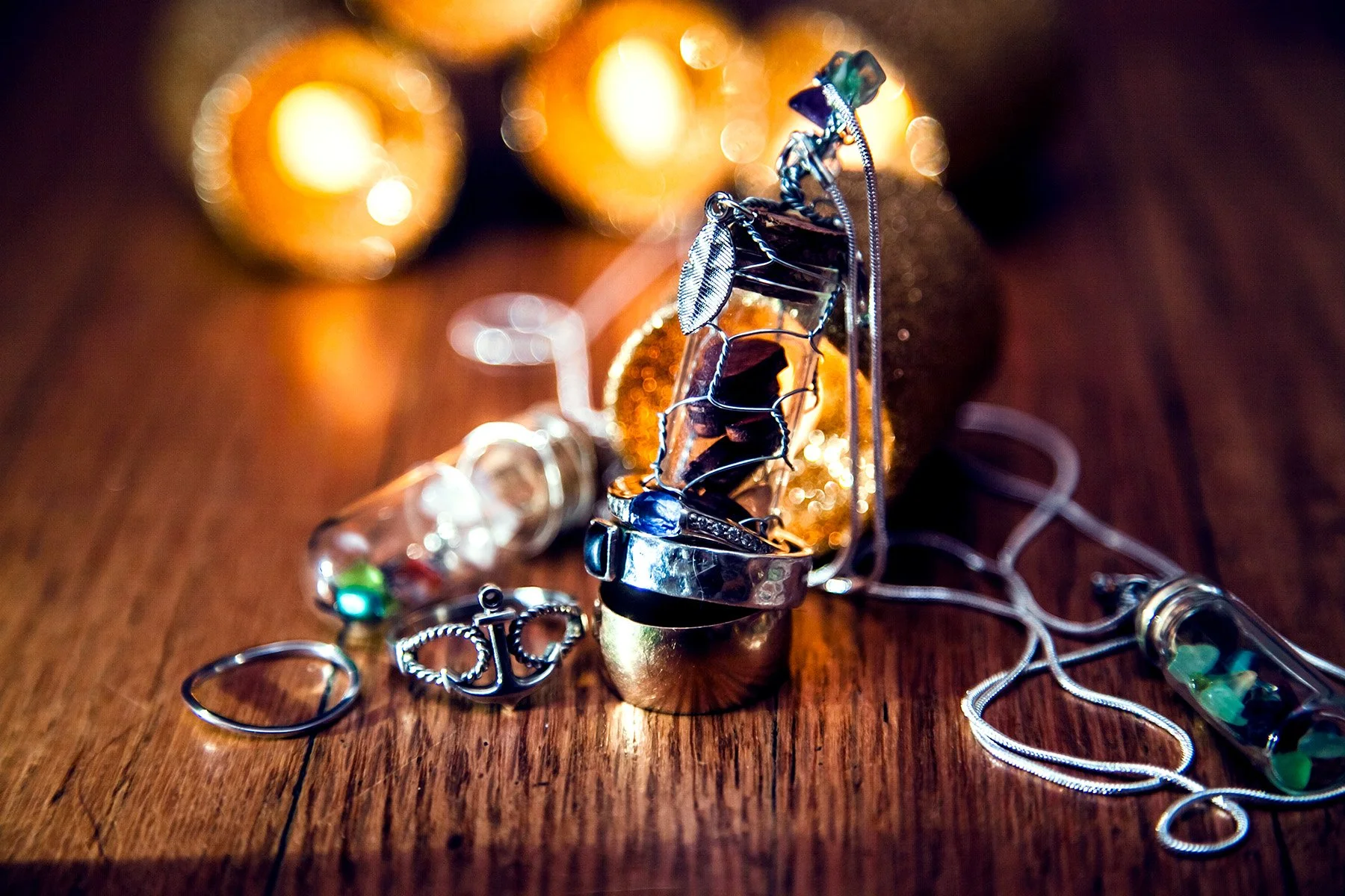 Close-up of various necklaces and jewelry pieces, including rings and chains, displayed on a wooden surface with warm lighting and blurred background.