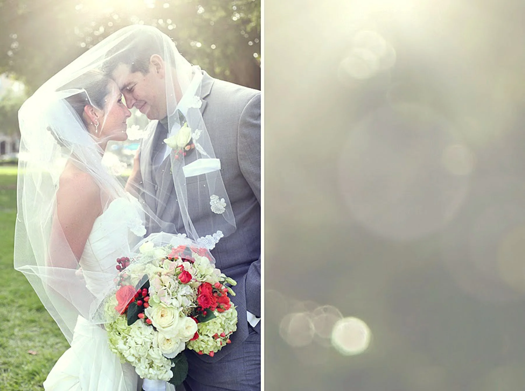 A bride and groom are standing close together outdoors, smiling with their foreheads touching under a sheer wedding veil. The bride is wearing a white wedding dress and holding a large bouquet of white, red, and green flowers. The groom is dressed in