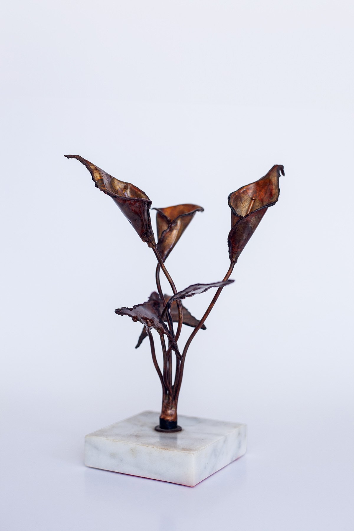 A metal sculpture of three brown, dried leaves on thin stems, mounted on a white marble base.