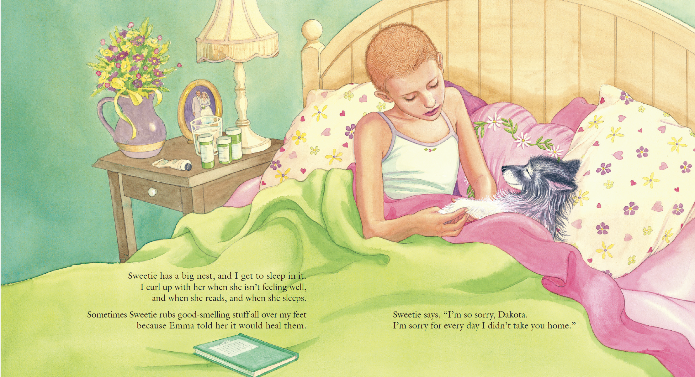 A young girl in a bed with pink and white floral pillows, holding her black and white dog named Dakota. The bed has a green blanket, and a nightstand with a vase of flowers, a clock, and medicine bottles. The room has pastel yellow and green walls.