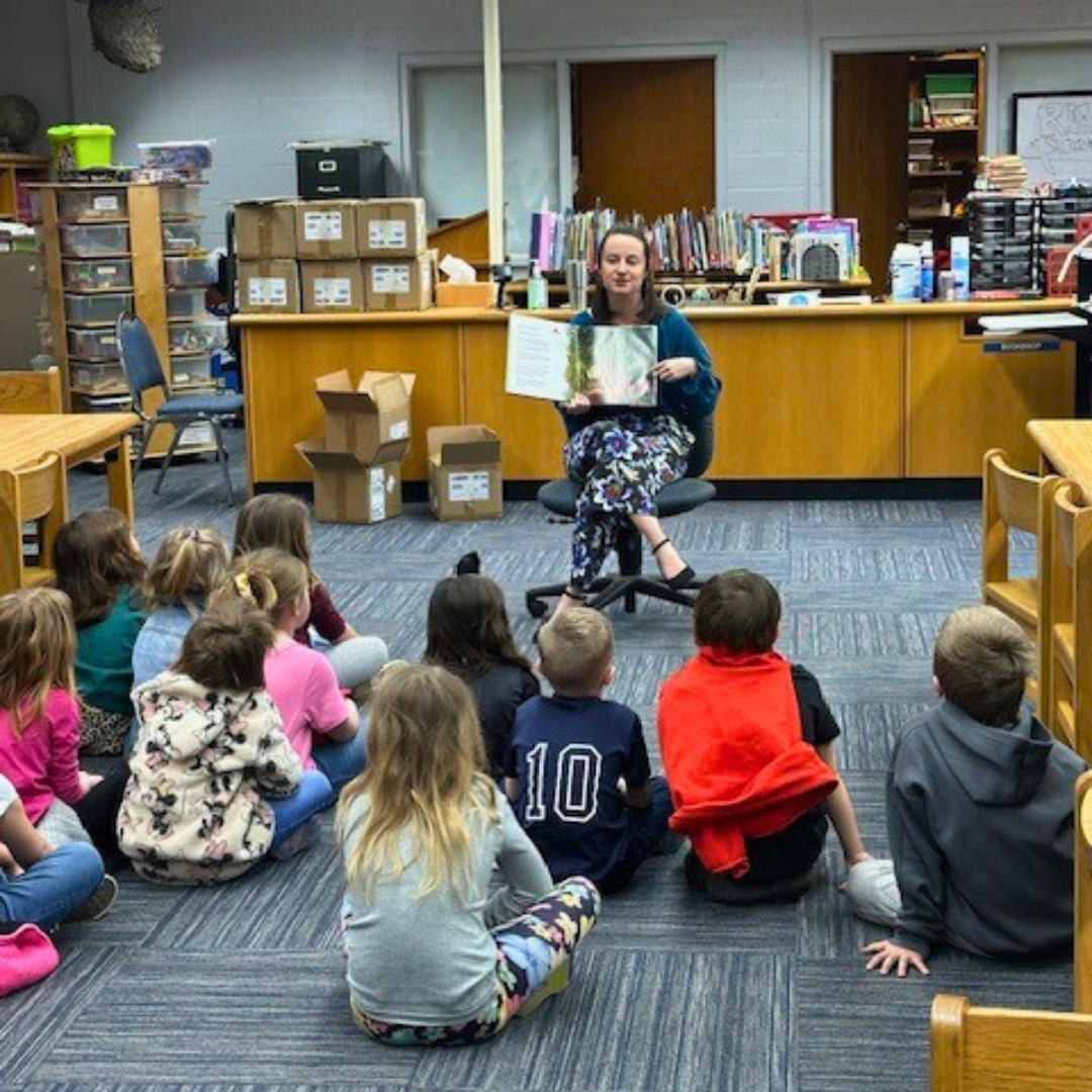 A woman reading a children's book to a group of kids sitting on the carpet in a library