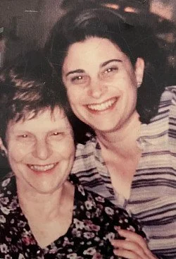 Two women smiling closely together, one appears older, the other younger, in a close-up photo.