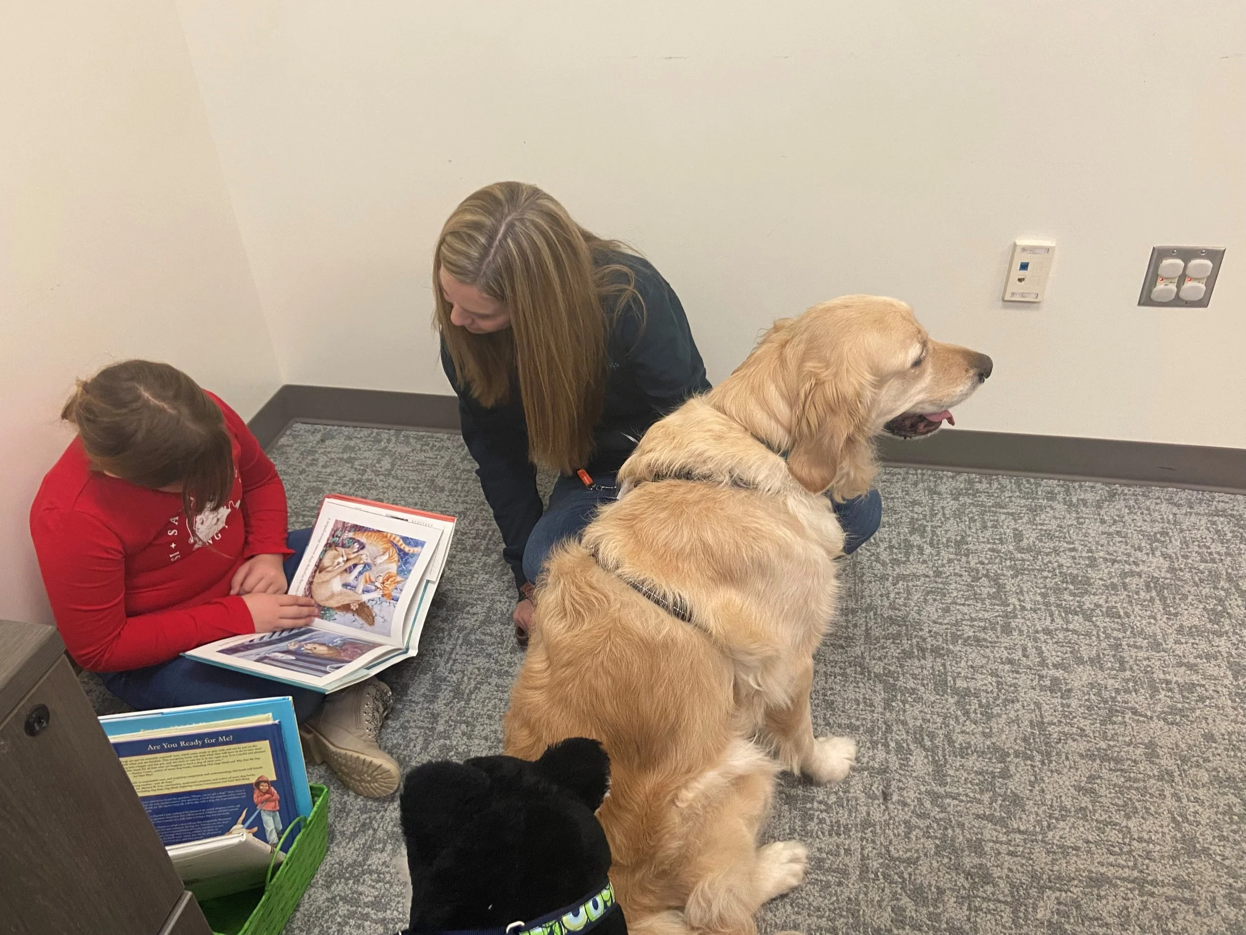 Woman and girl reading a book on the floor with a dog nearby.