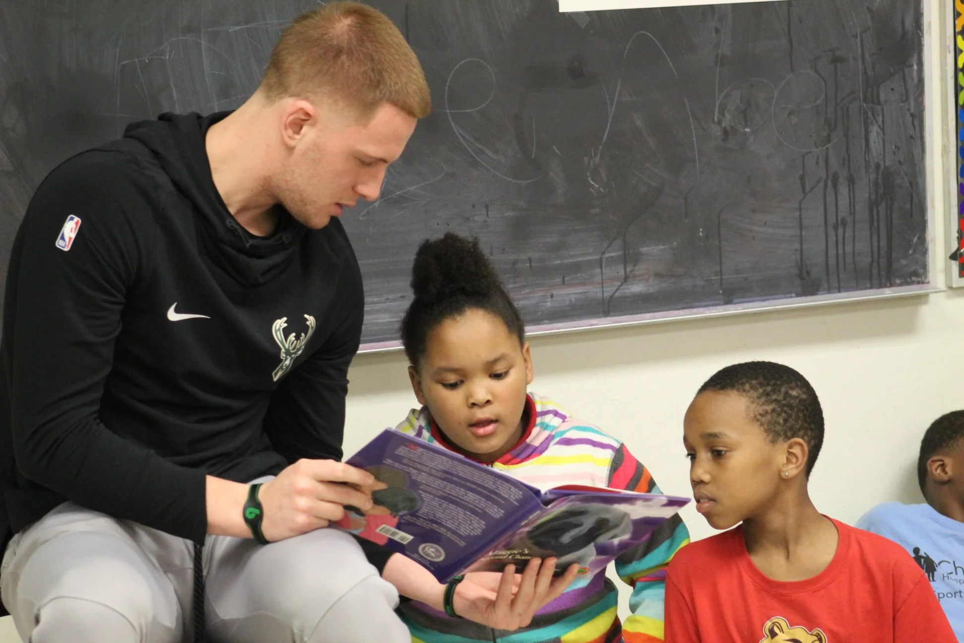 A man and three children sitting in front of a blackboard, looking at a book.