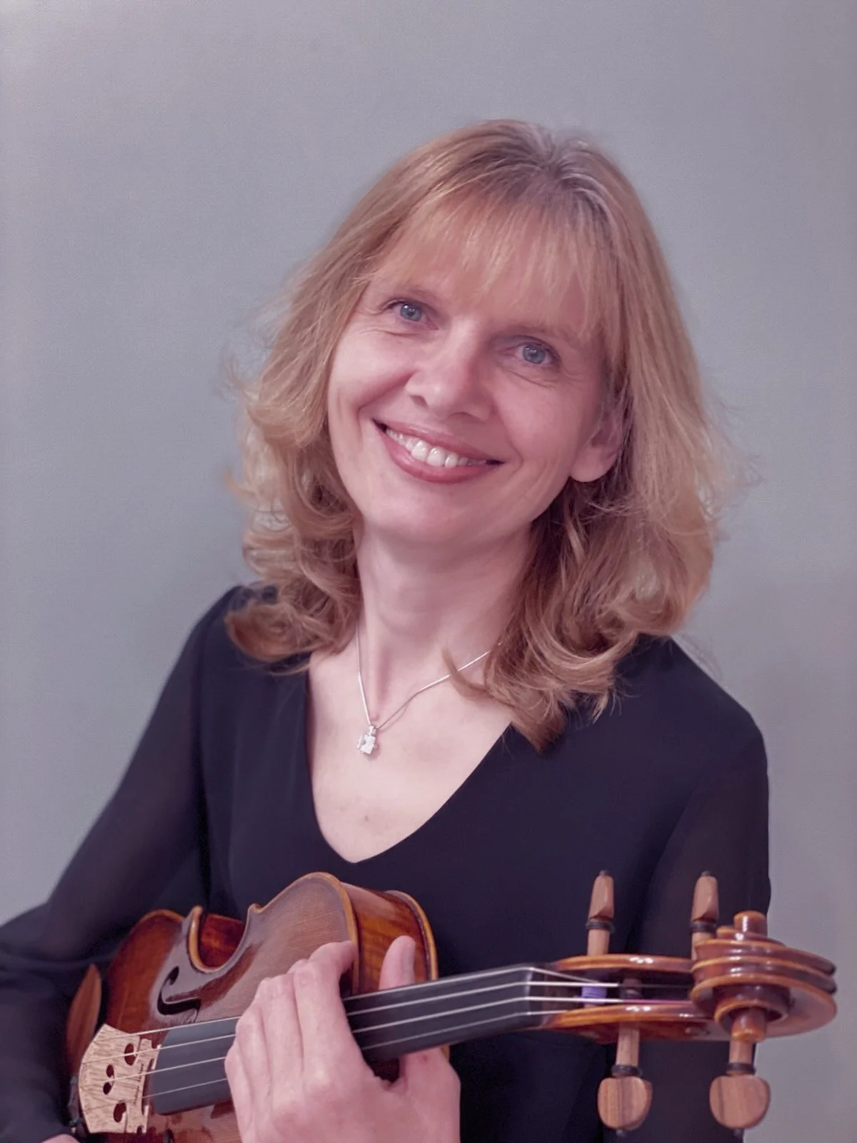 A professional female musician with shoulder-length blonde hair holding a viola and smiling at the camera.