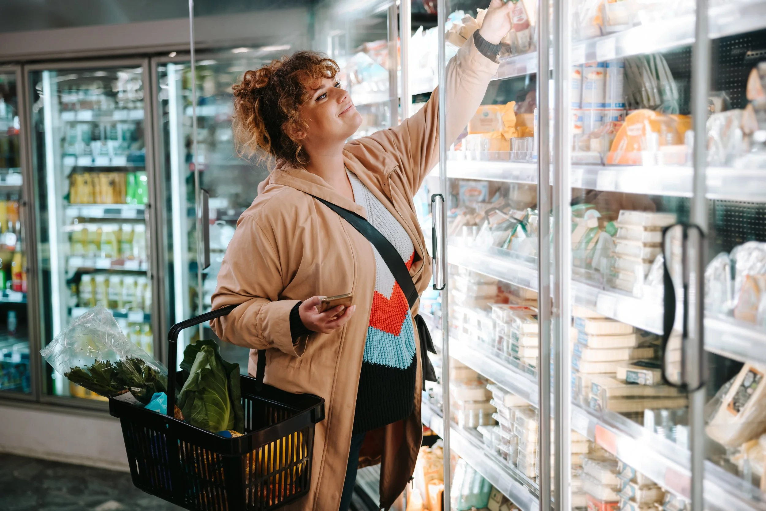 Young white woman grocery shopping, reaching into a refrigerator case