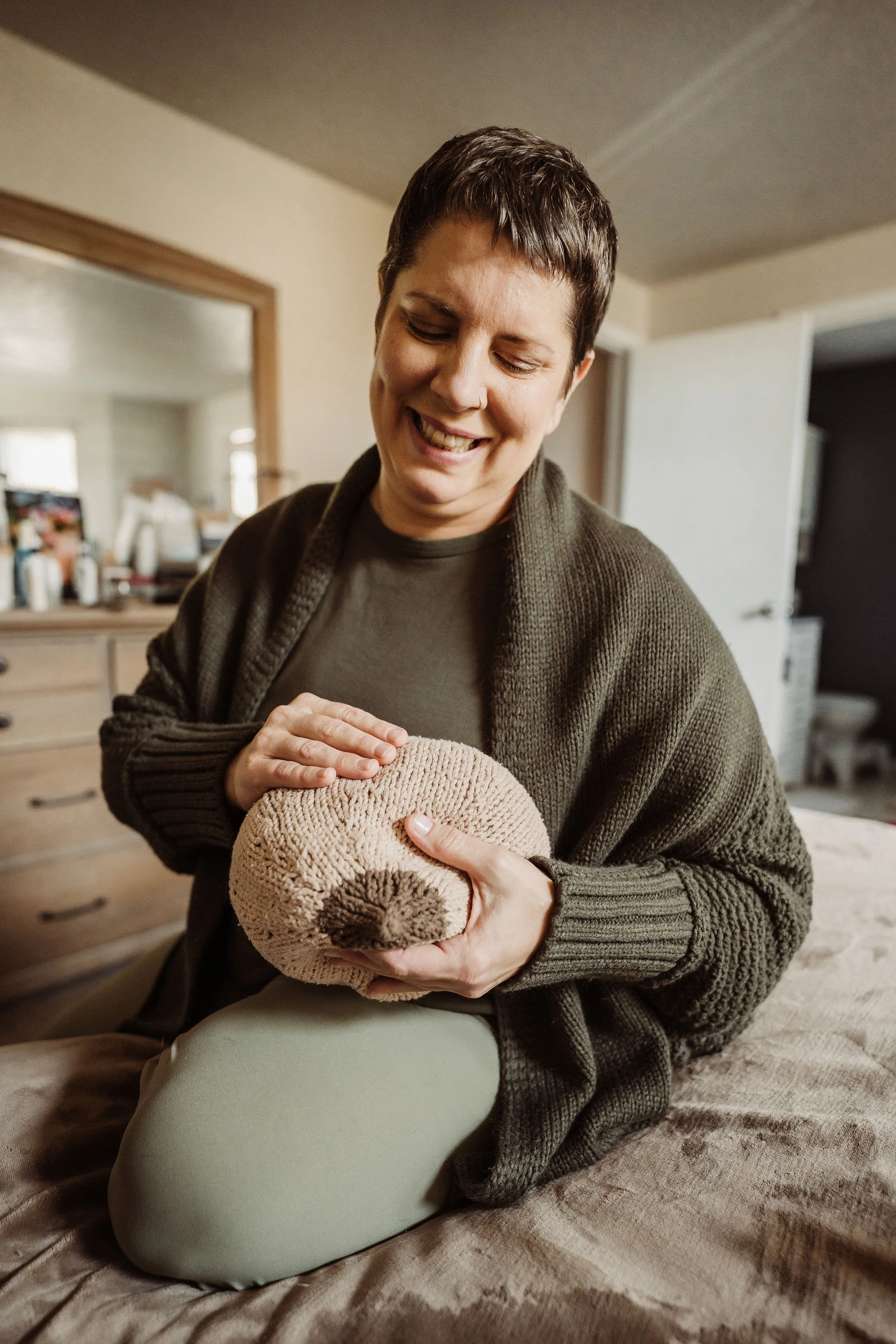 A woman with tattoos and a tattoo on her thigh breastfeeds a baby in bed.