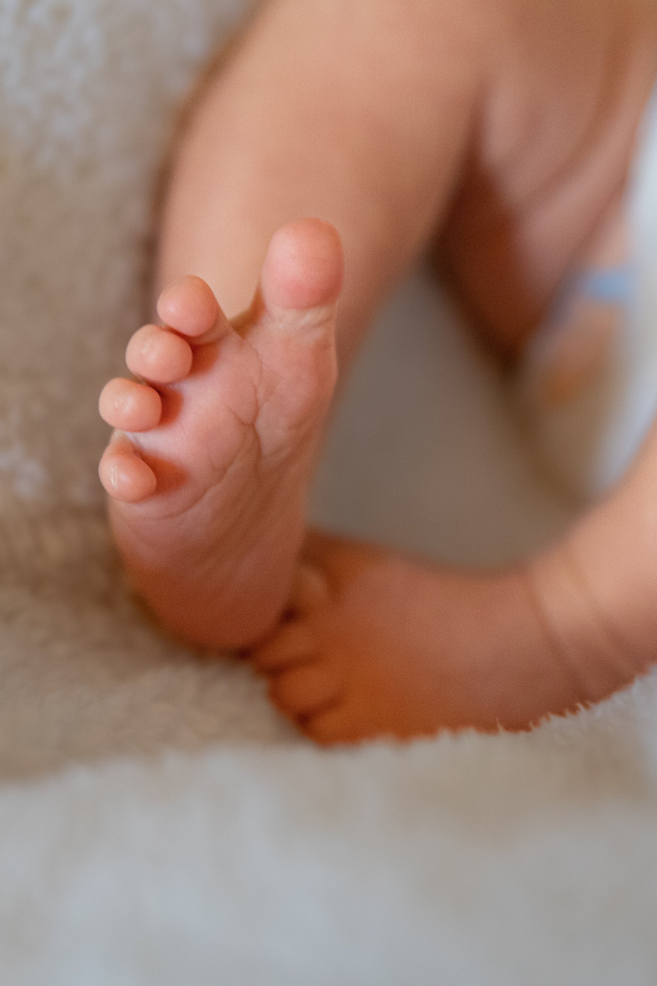 Close-up of a baby's tiny foot and toes on a soft, light-colored surface.