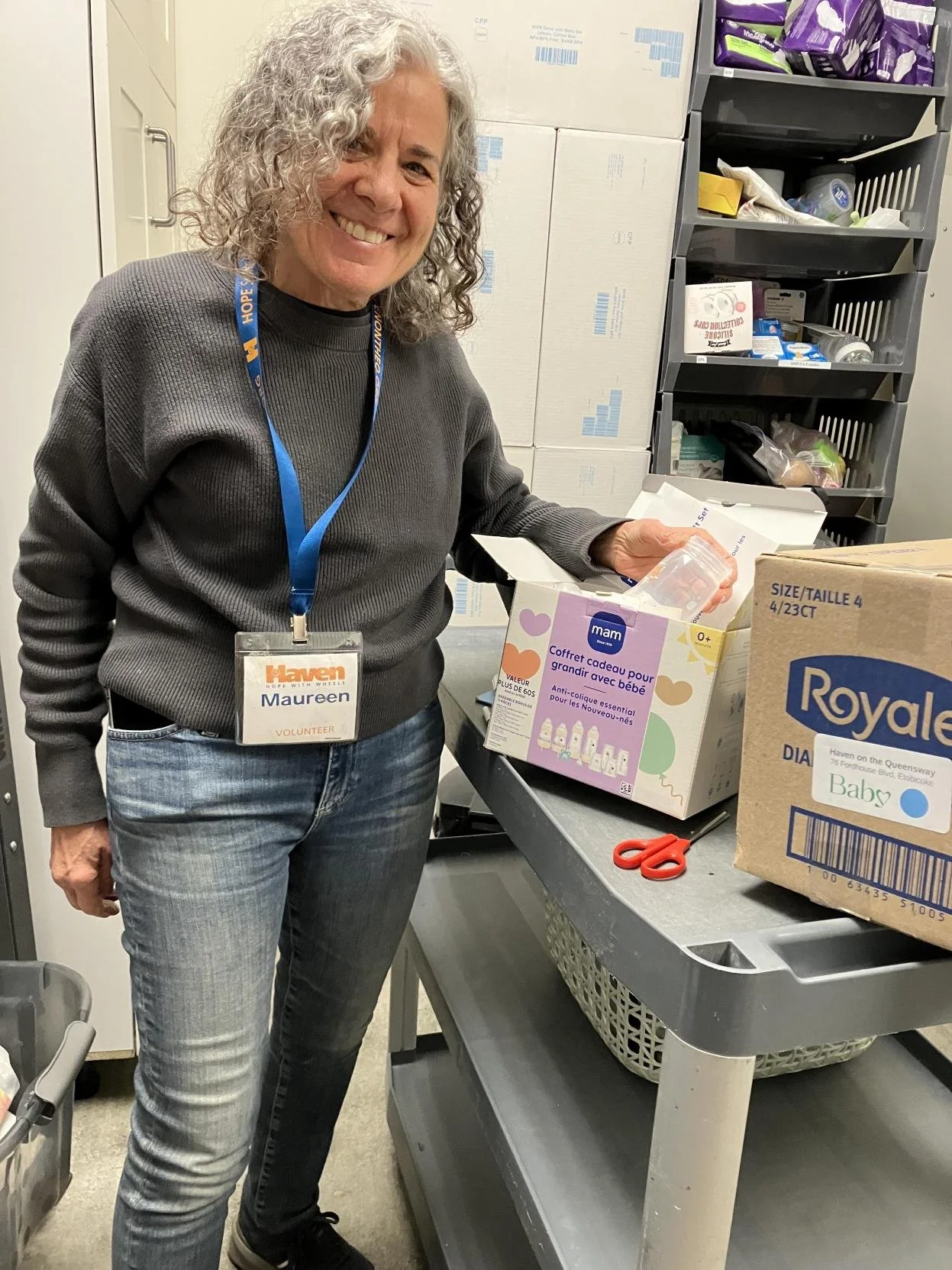 Haven on the Queensway staff member showcases a box of Royale diapers and a MAM bottle gift set received from Baby Love