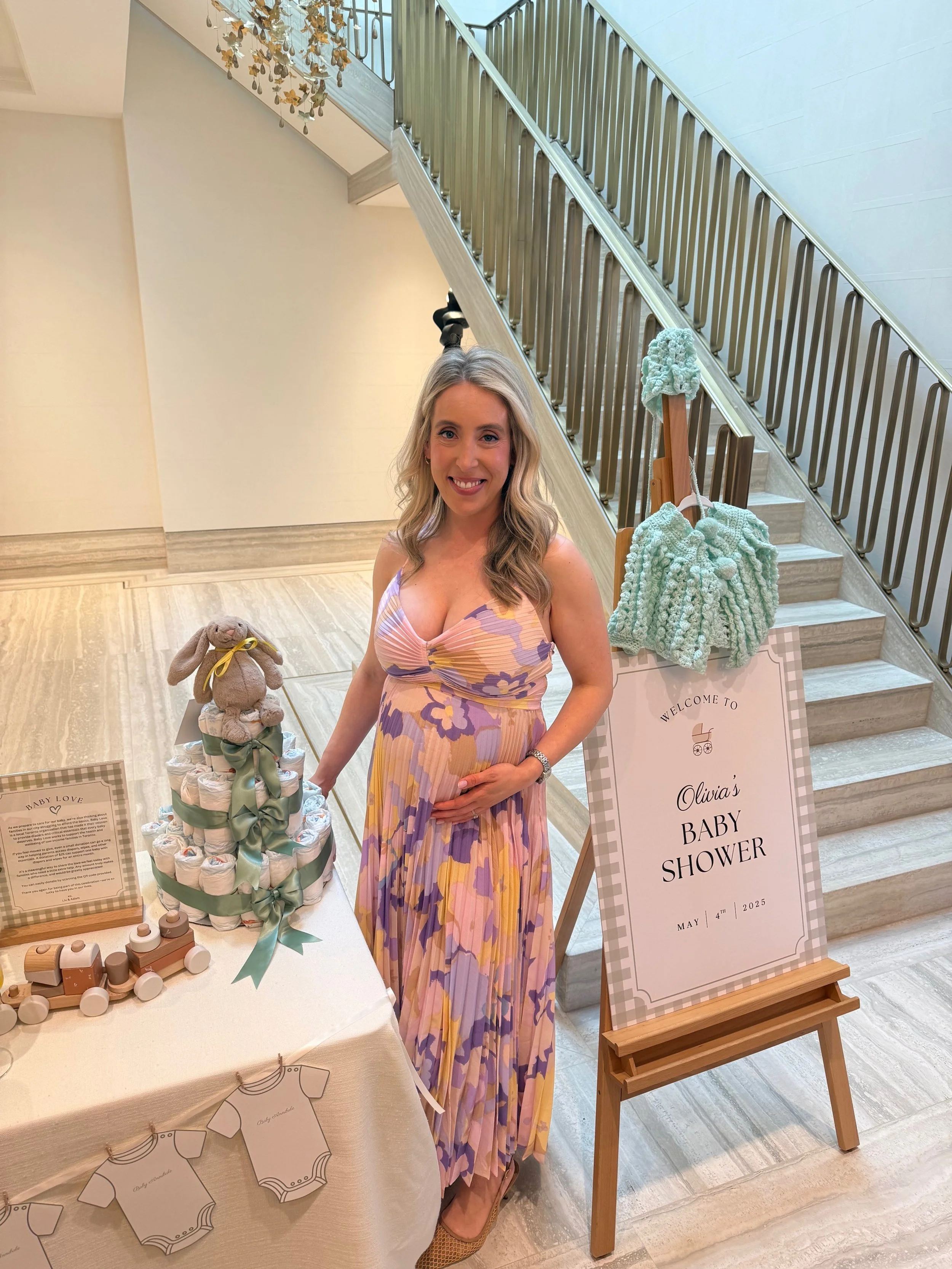 An expectant mom is shown in front of a Baby Love diaper cake from her baby shower which served as a fundraiser for Baby Love