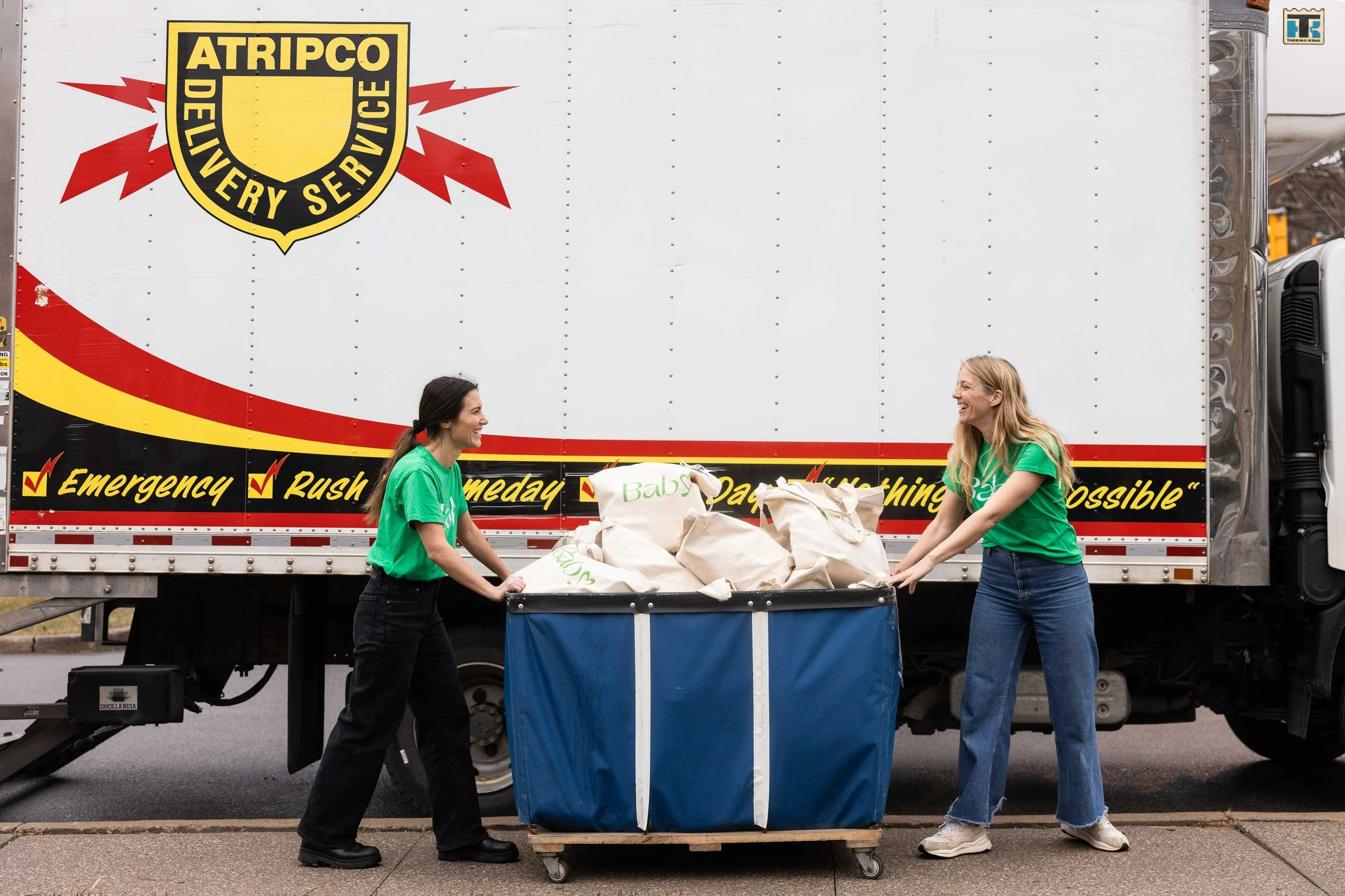 Two Baby Love volunteers are shown moving Baby Love gift bags in front of an Atripco delivery truck