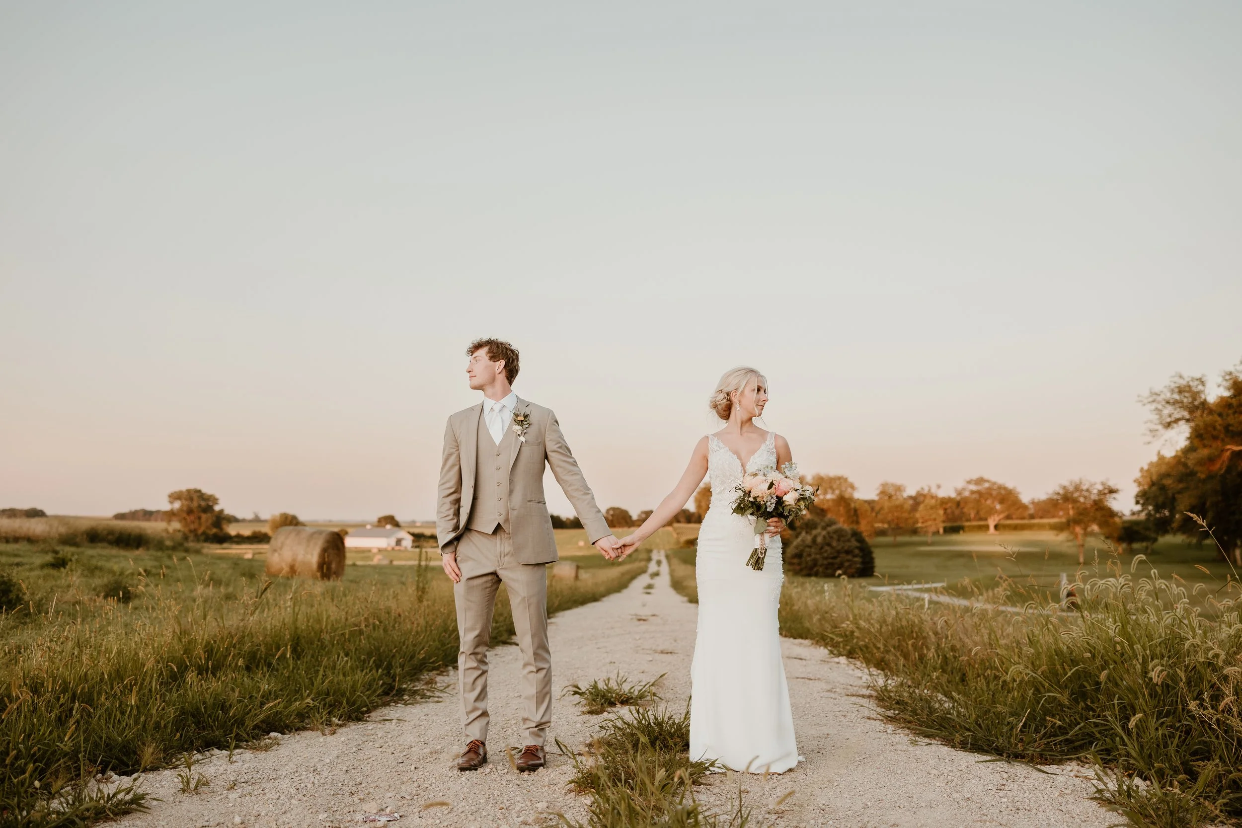 Wedding couple holding hands on a country dirt road at sunset