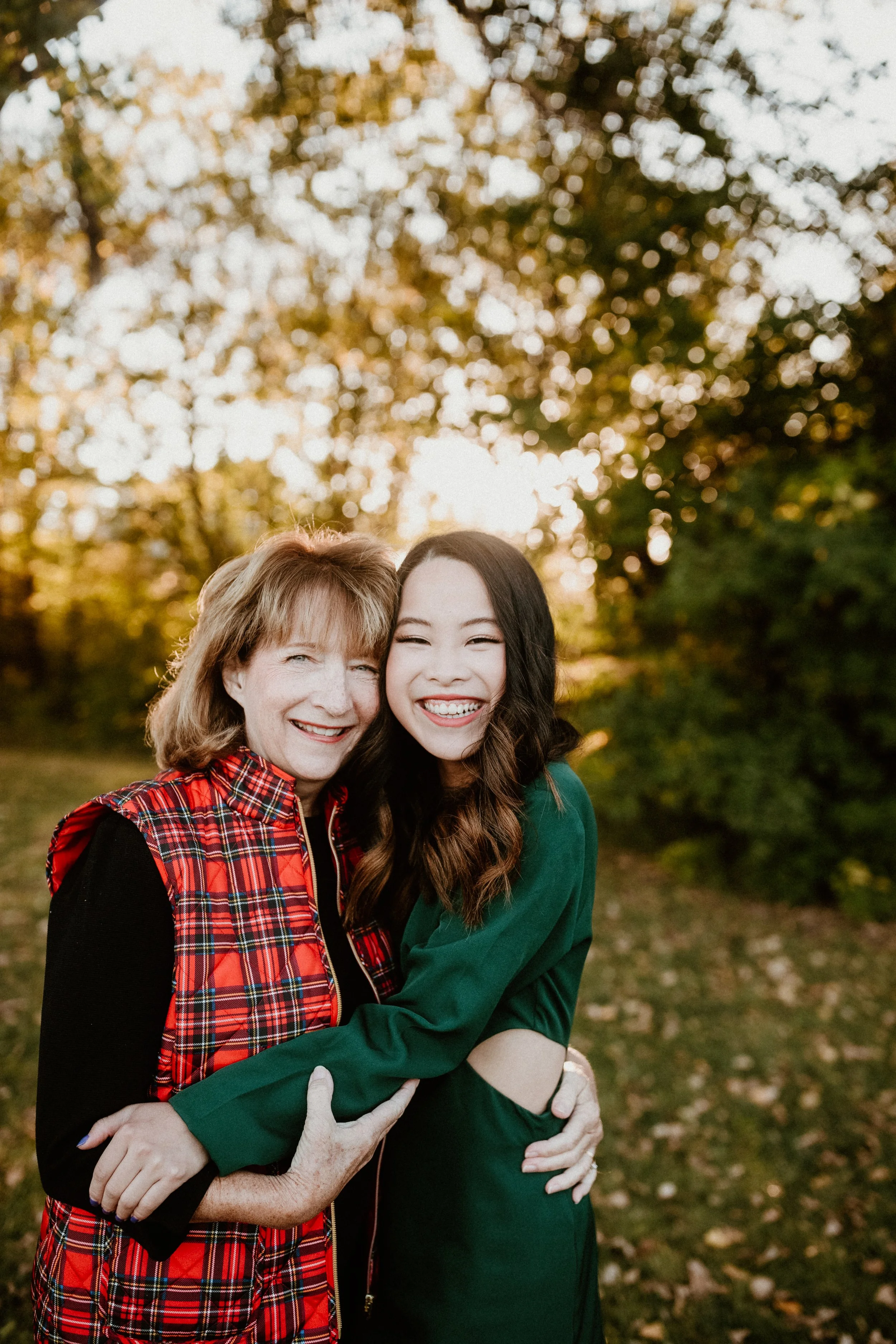Two women hugging outdoors during fall, smiling, with trees and fall leaves in the background.
