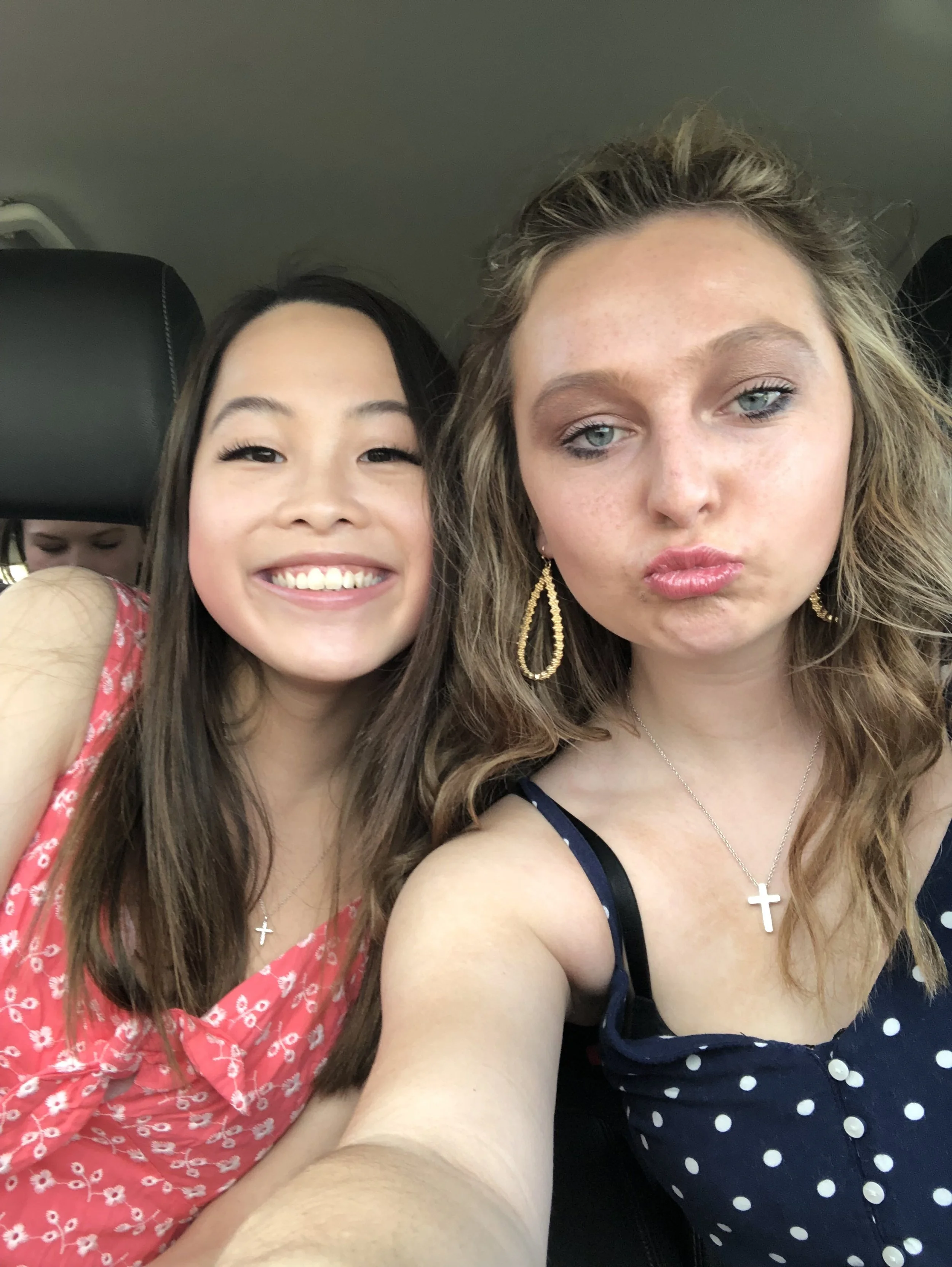 Two women taking a selfie inside a car, one smiling and the other making a pouty face.