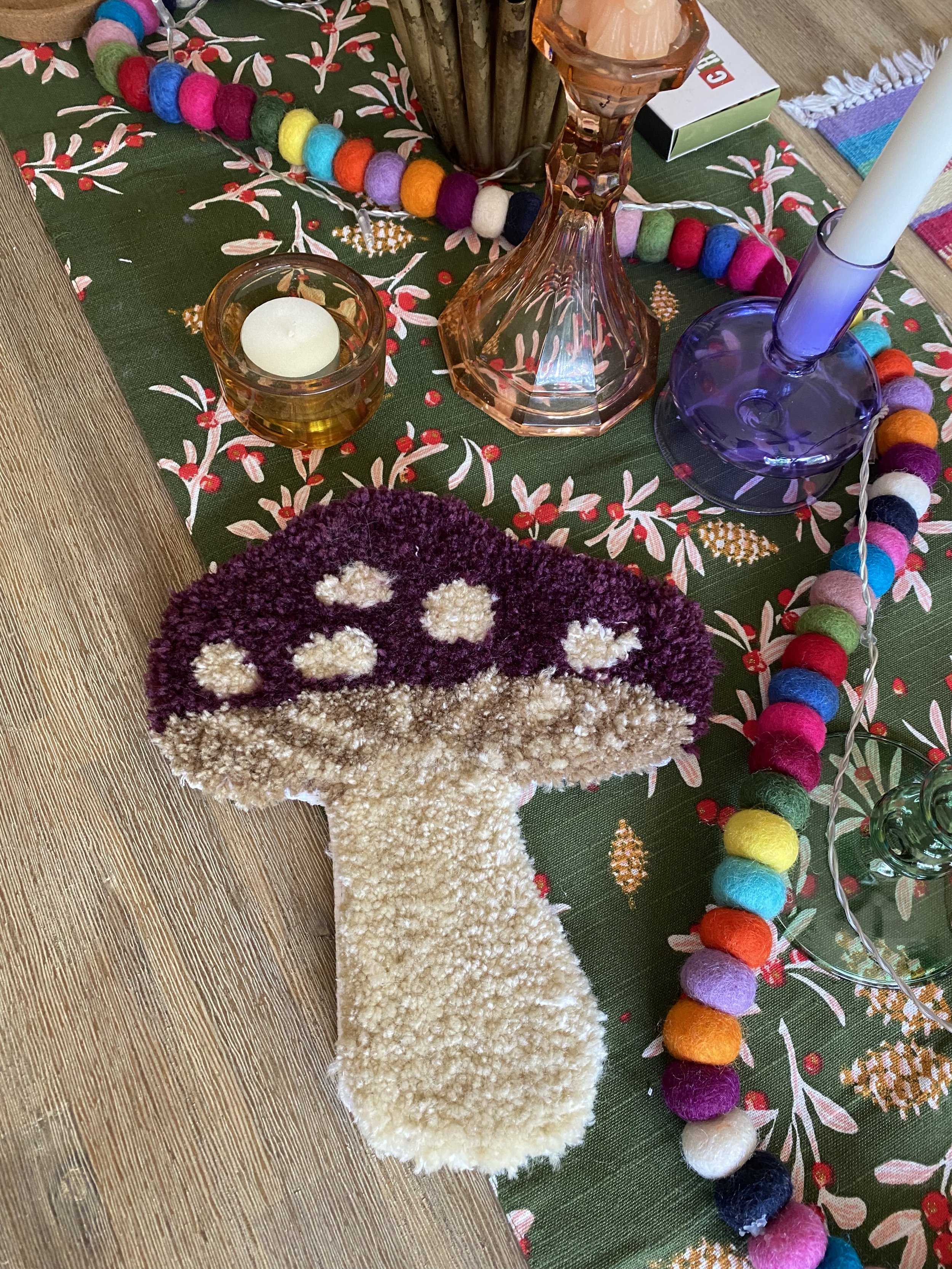 Colorful felt mushroom decoration on a decorated table with candles and colorful felt ball garland.