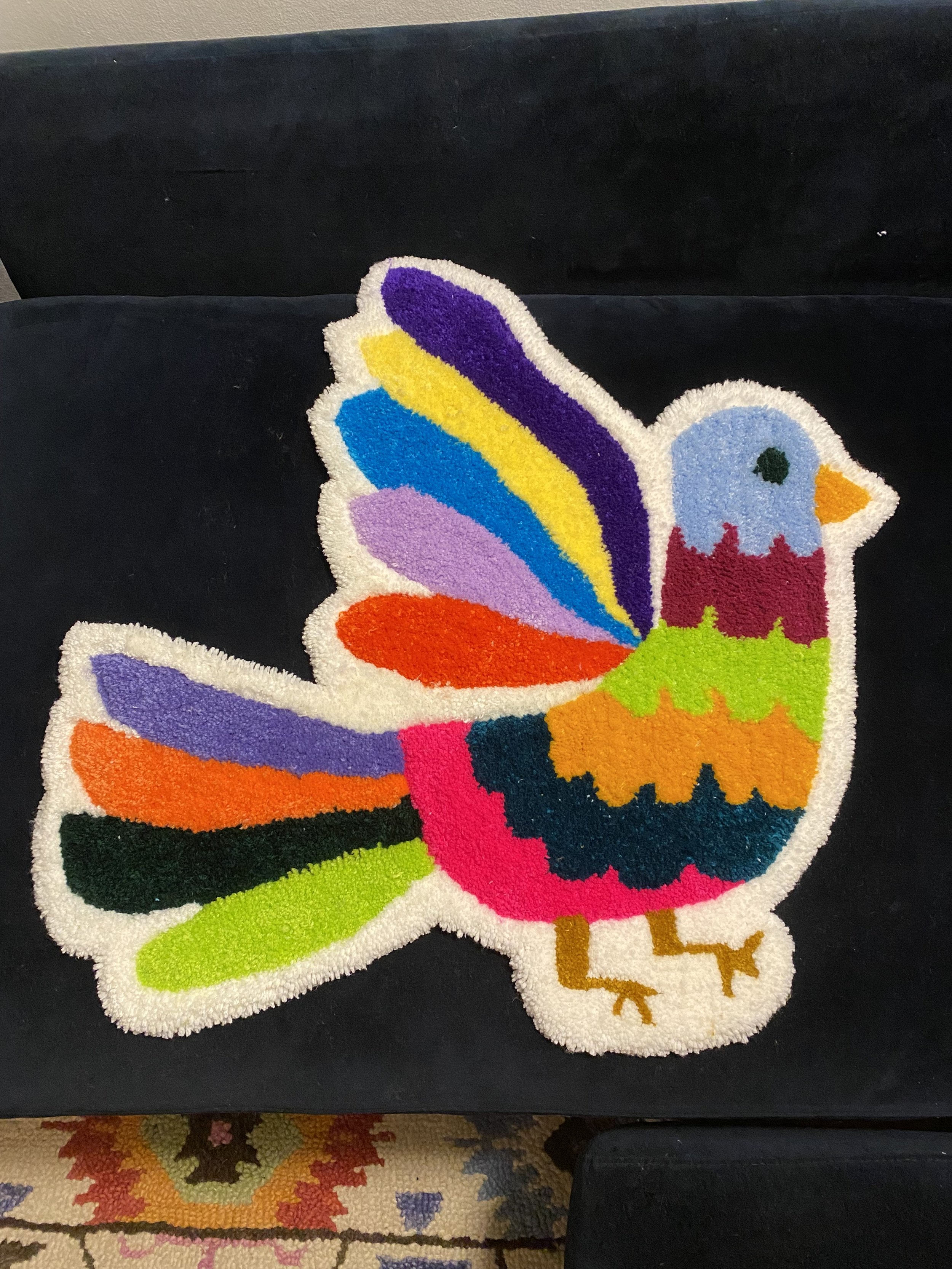 Colorful, rainbow-patterned depiction of a bird, possibly a rooster, with a rainbow tail, rainbow feathers on its wings, a blue face, red crest, and yellow legs, on a black background.