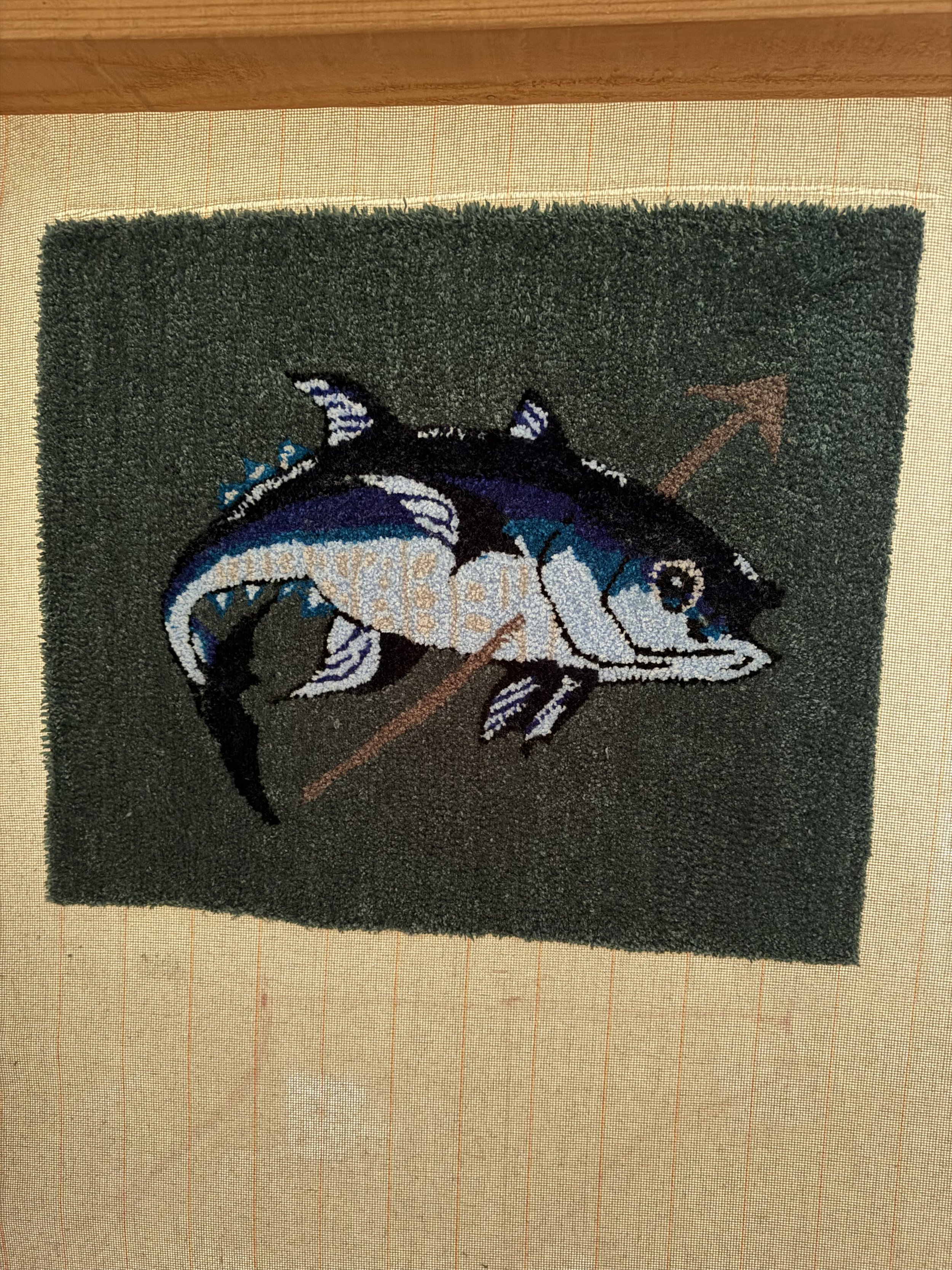 A decorated doormat featuring a shark with a fishing hook, on a square-shaped black background.