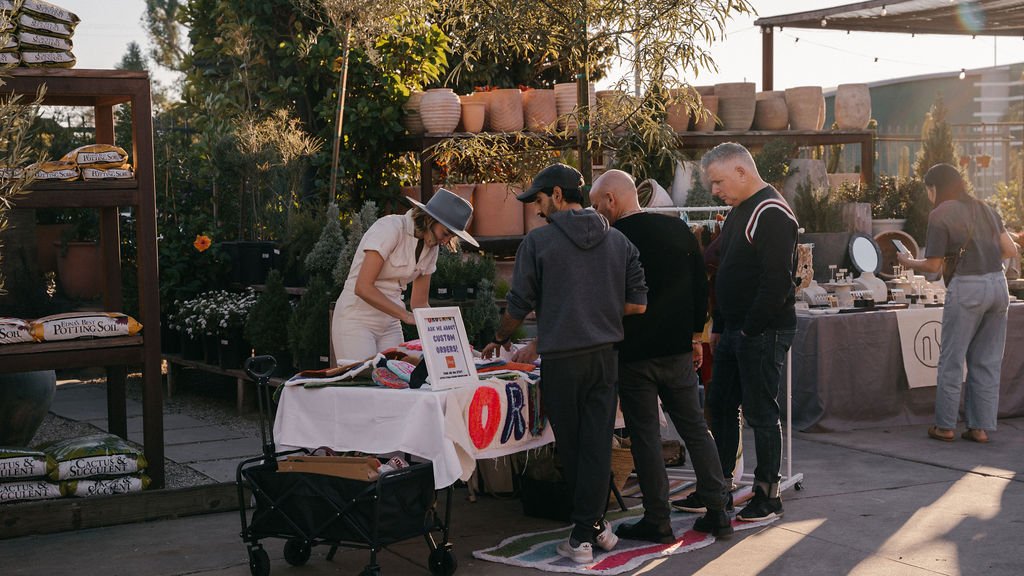 People shopping at an outdoor market with plants and pottery displays.