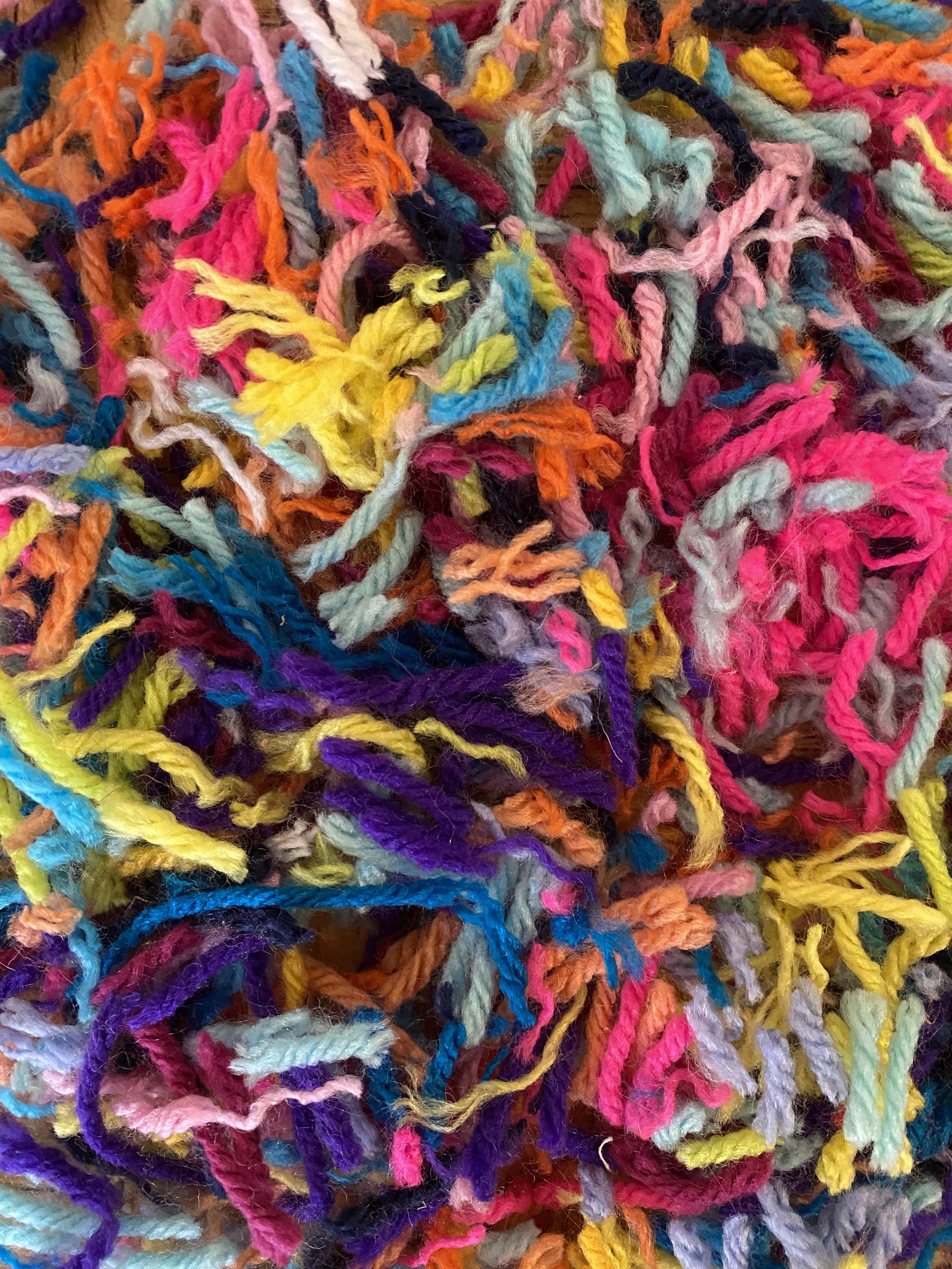 Close-up of multicolored, tangled yarn fibers in shades of pink, blue, yellow, purple, orange, and black.