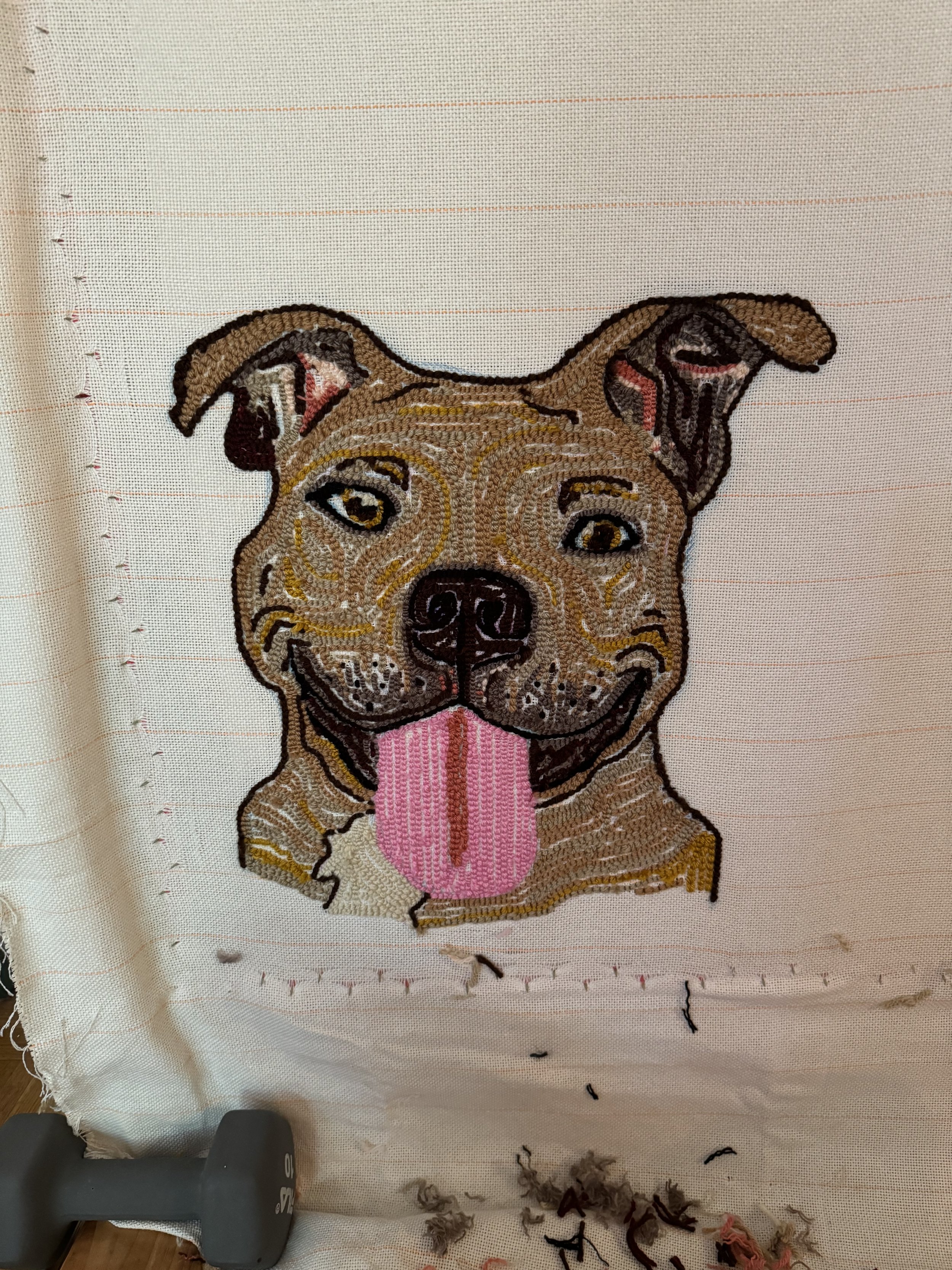 Embroidery of a smiling dog with its tongue out on a white fabric background.
