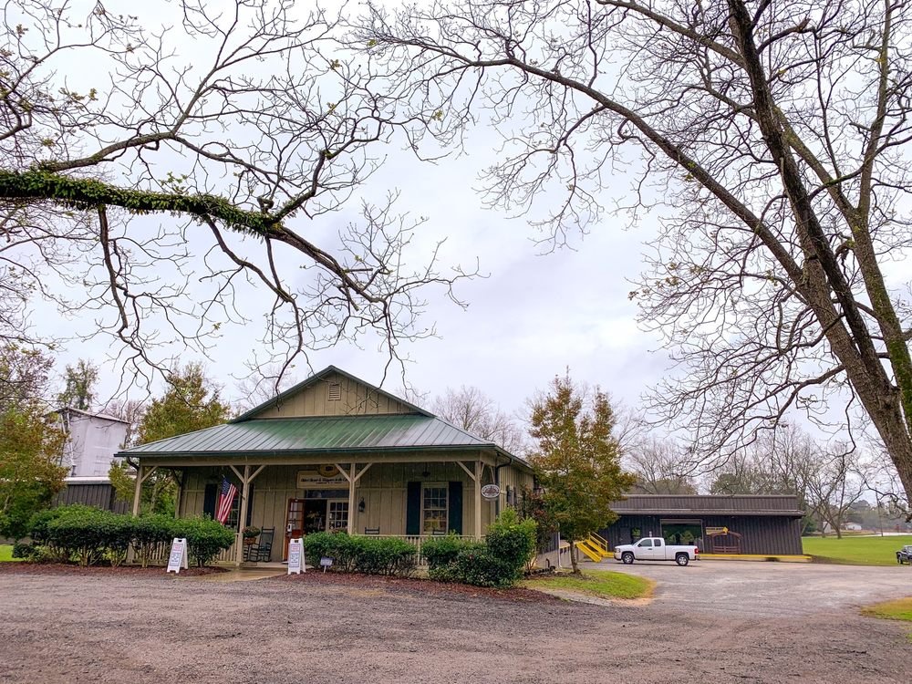 The Golden Kernel Pecan Co store in South Carolina. It's a rustic building with a metal roof and a porch, decorated with an American flag, set in a rural area with trees and parked vehicles.
