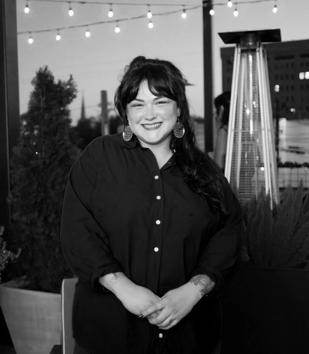 A beautiful, smiling woman with bangs and big earrings in a button-up top with a party happening in the background. She is a happy astrocartography client whose testimonial is written below.