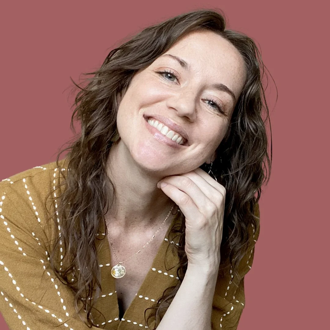 Certified Locational Astrologer and Astrocartographer Charlie with Celestia Terra who is a smiling woman with wavy brown hair wearing a dark chartreuse dress with embroidered off-white lines and a flower necklace on an earthy, muted red background.