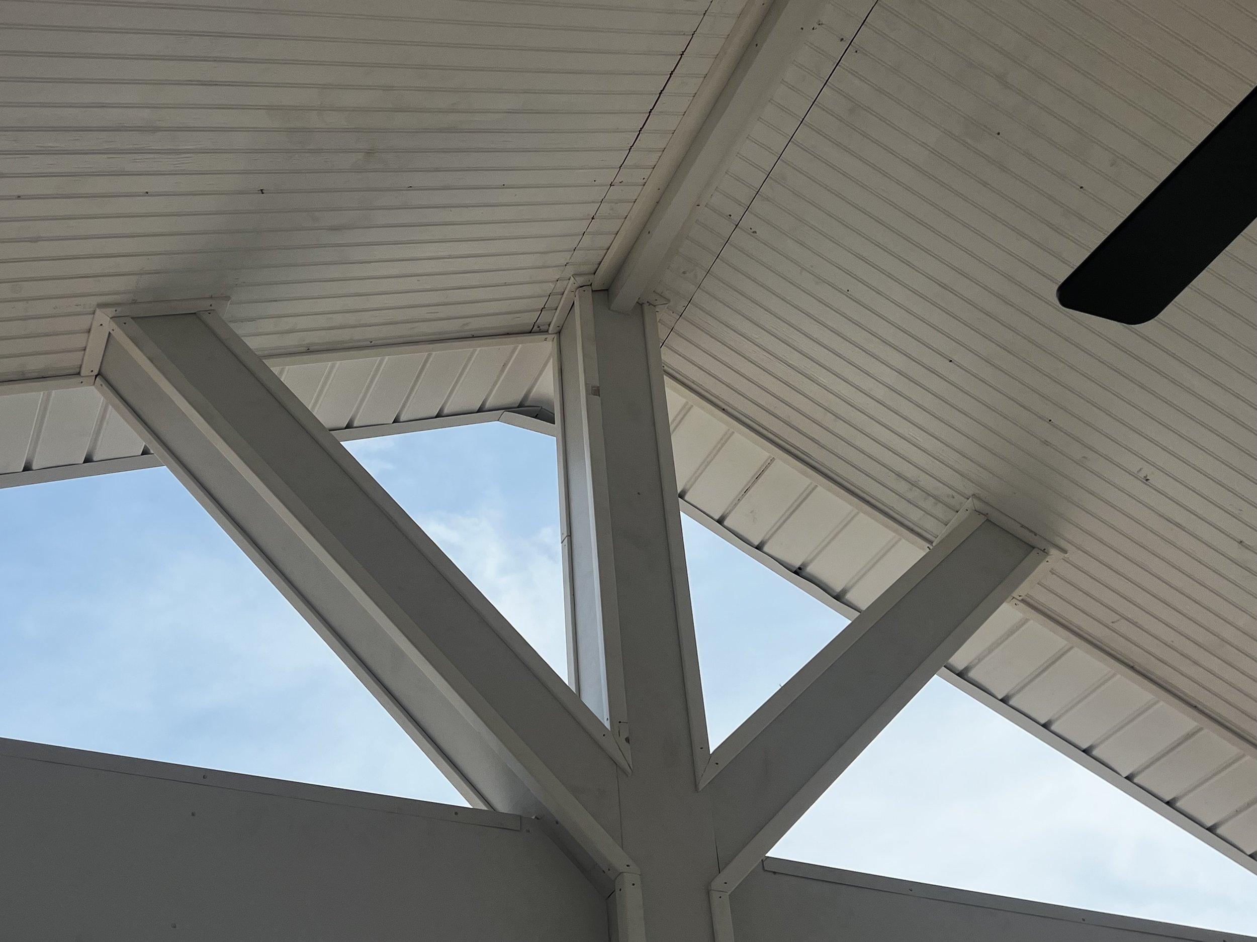 Close-up of a corner of a house's roof with beige siding, white trim, and a black vent, with a view of the blue sky through the opening.