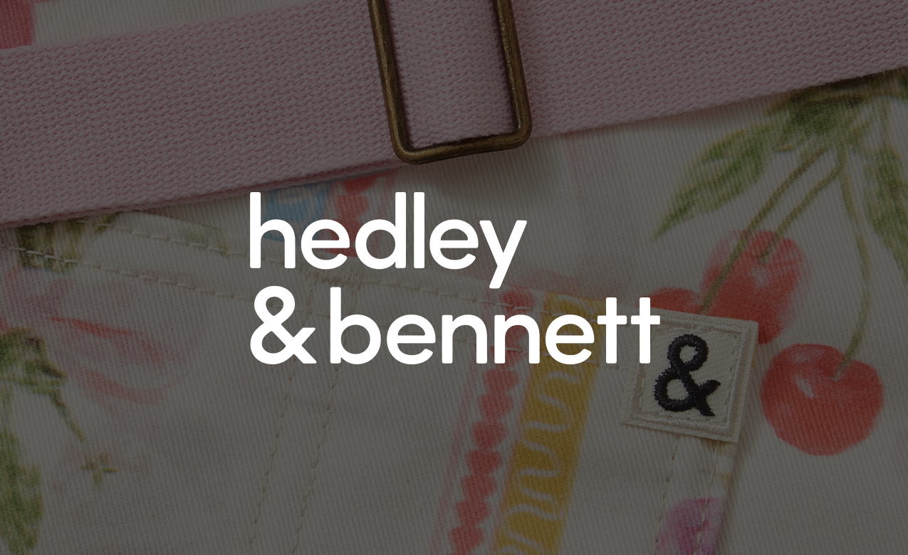 Close-up of a fabric with a cherry print, a pink fabric belt, and a clothing label with an ampersand symbol.