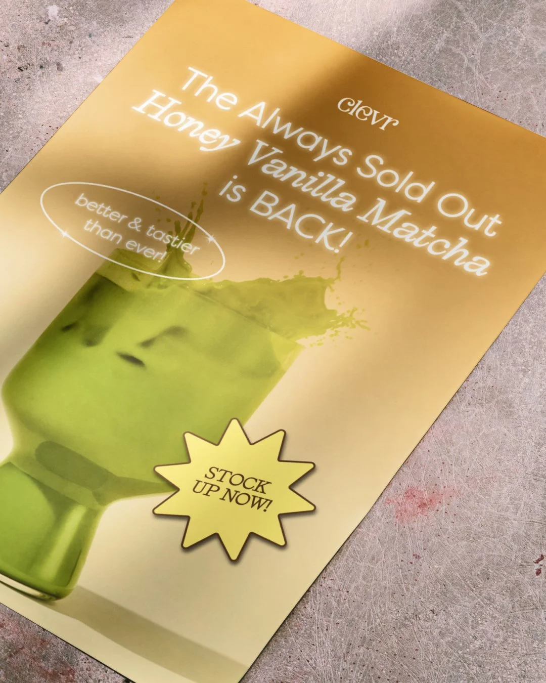 Flyer advertising honey vanilla matcha, with a picture of a green matcha drink in a glass, splashing out, and a yellow starburst that says 'Stock Up Now!'. The flyer states that the honey vanilla matcha is always sold out and is back, with a tagline 
